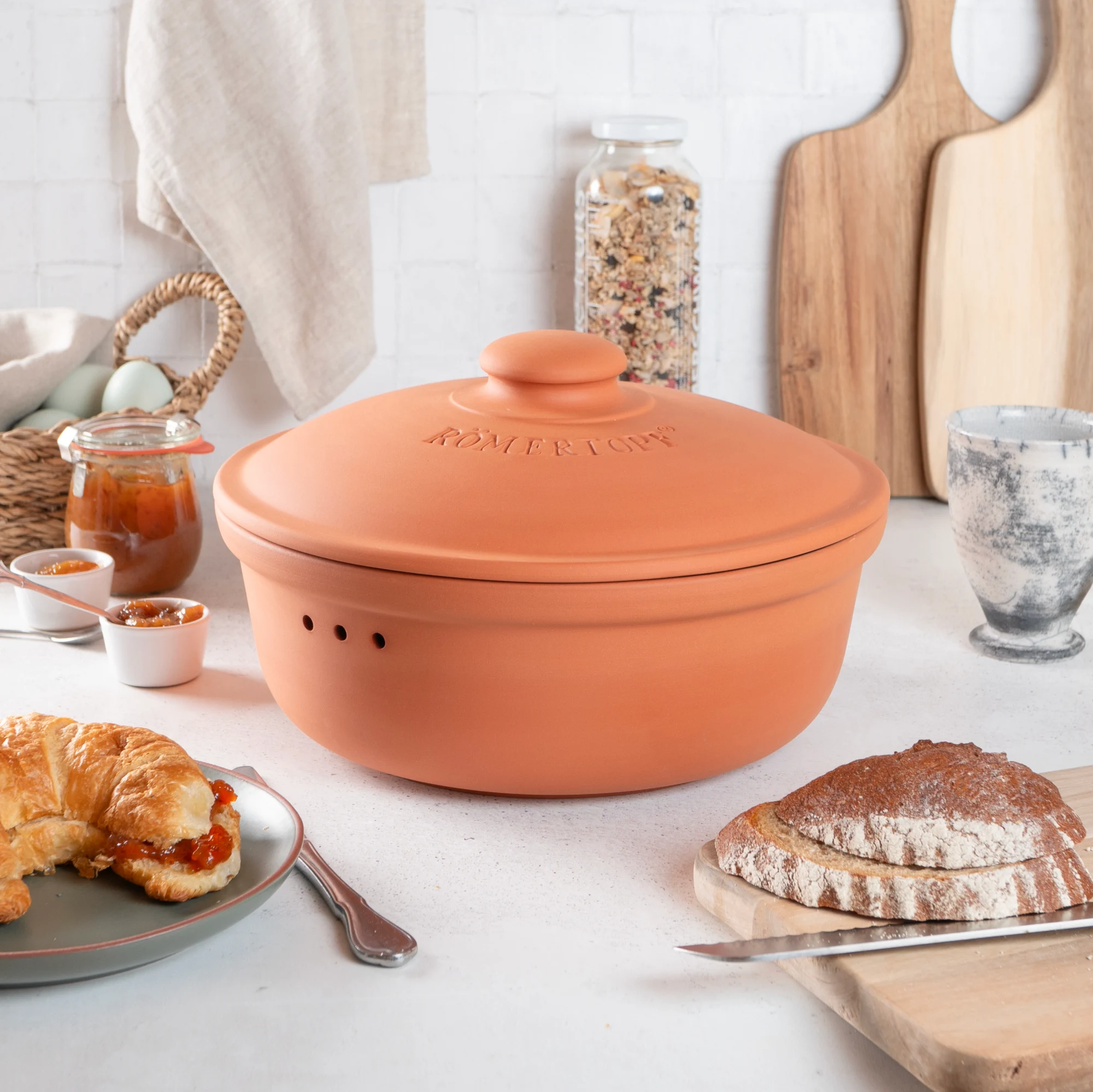 Römertopf Brottopf rund aus Terracotta – Frischetopf zur optimalen Aufbewahrung von Brot Runder Brottopf aus Terrakotta mit eingeprägtem „Römertopf“-Schriftzug auf dem Deckel, belüftete Seitenteile zur Frischebewahrung, auf weißem Hintergrund.