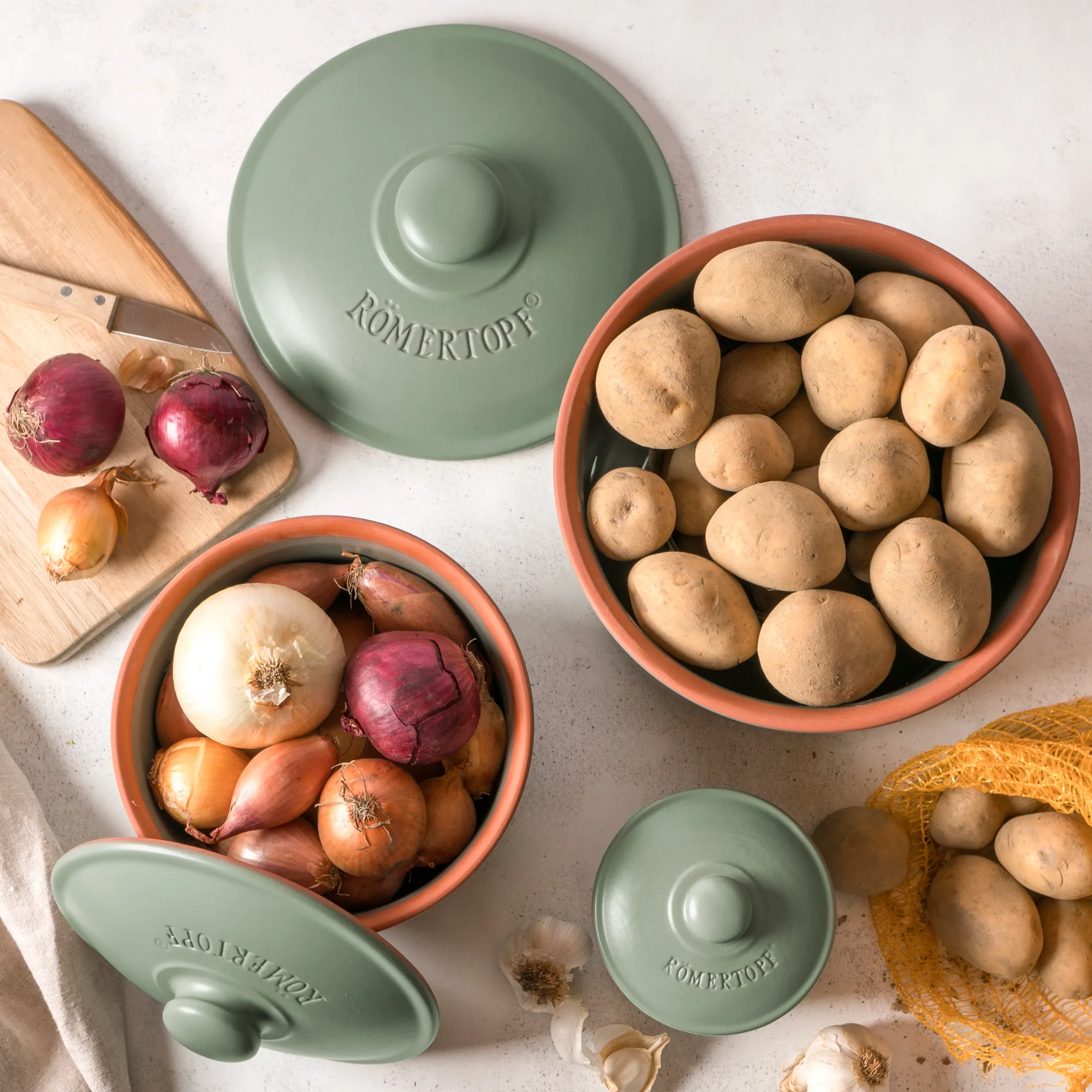 Römertopf Vorratstopf Set grün – 3-teiliges Keramikbehälter-Set zur Aufbewahrung von Lebensmitteln Vorratsgefäß-Set aus grün glasierter Keramik von Römertopf, bestehend aus drei unterschiedlich großen Töpfen mit passendem Deckel, jeweils mit geprägtem Schriftzug für Mehl, Zucker und Salz, stehend auf einer neutralen Oberfläche.
