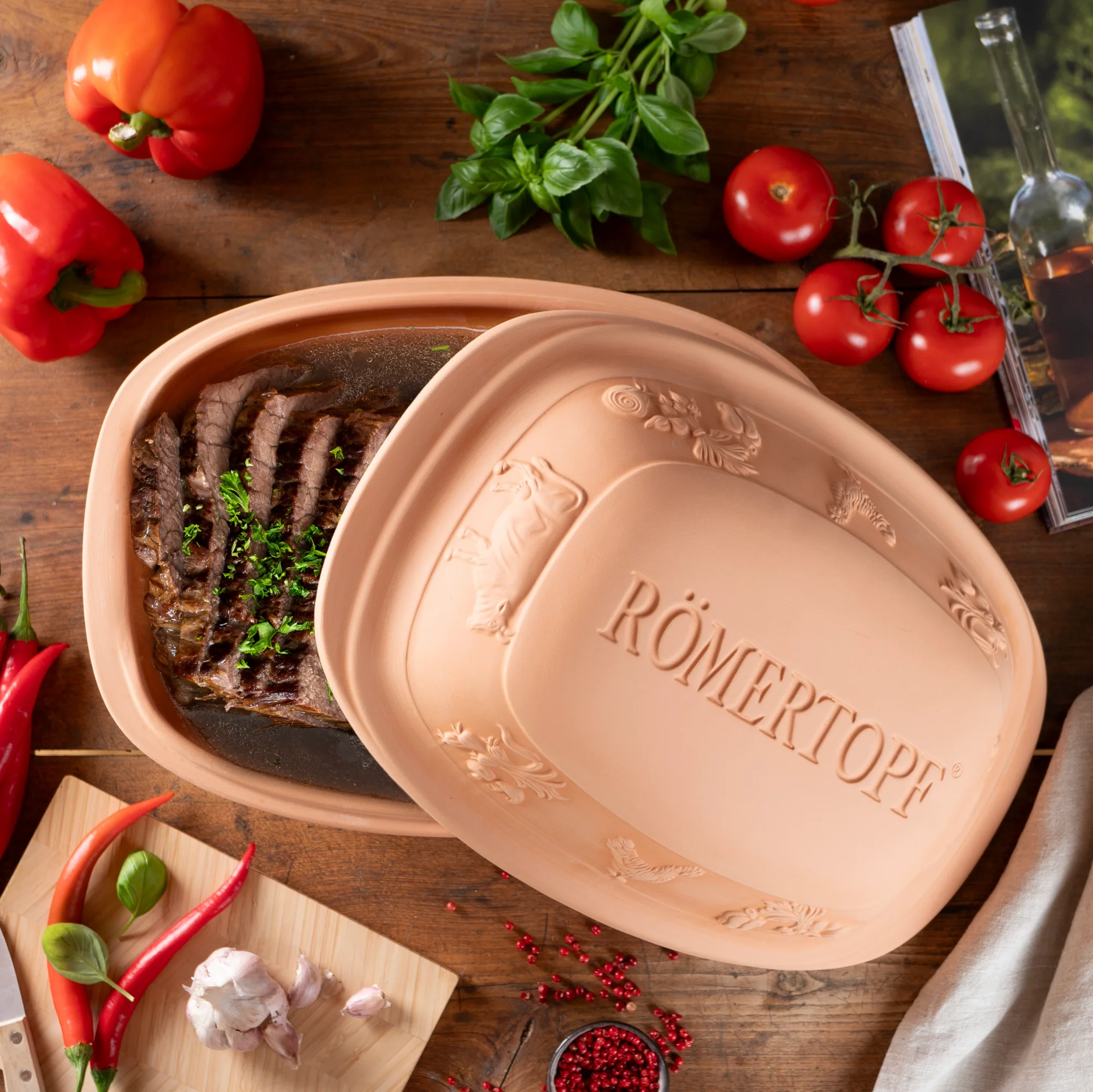Römertopf Rustico für 6 Personen aus Terracotta – klassischer Bräter für schonendes Garen Terrakotta-Bräter „Römertopf Rustico“ für 6 Personen mit rechteckiger Form, leicht gewölbtem Deckel und eingeprägtem Schriftzug „RÖMERTOPF“, auf weißem Hintergrund.