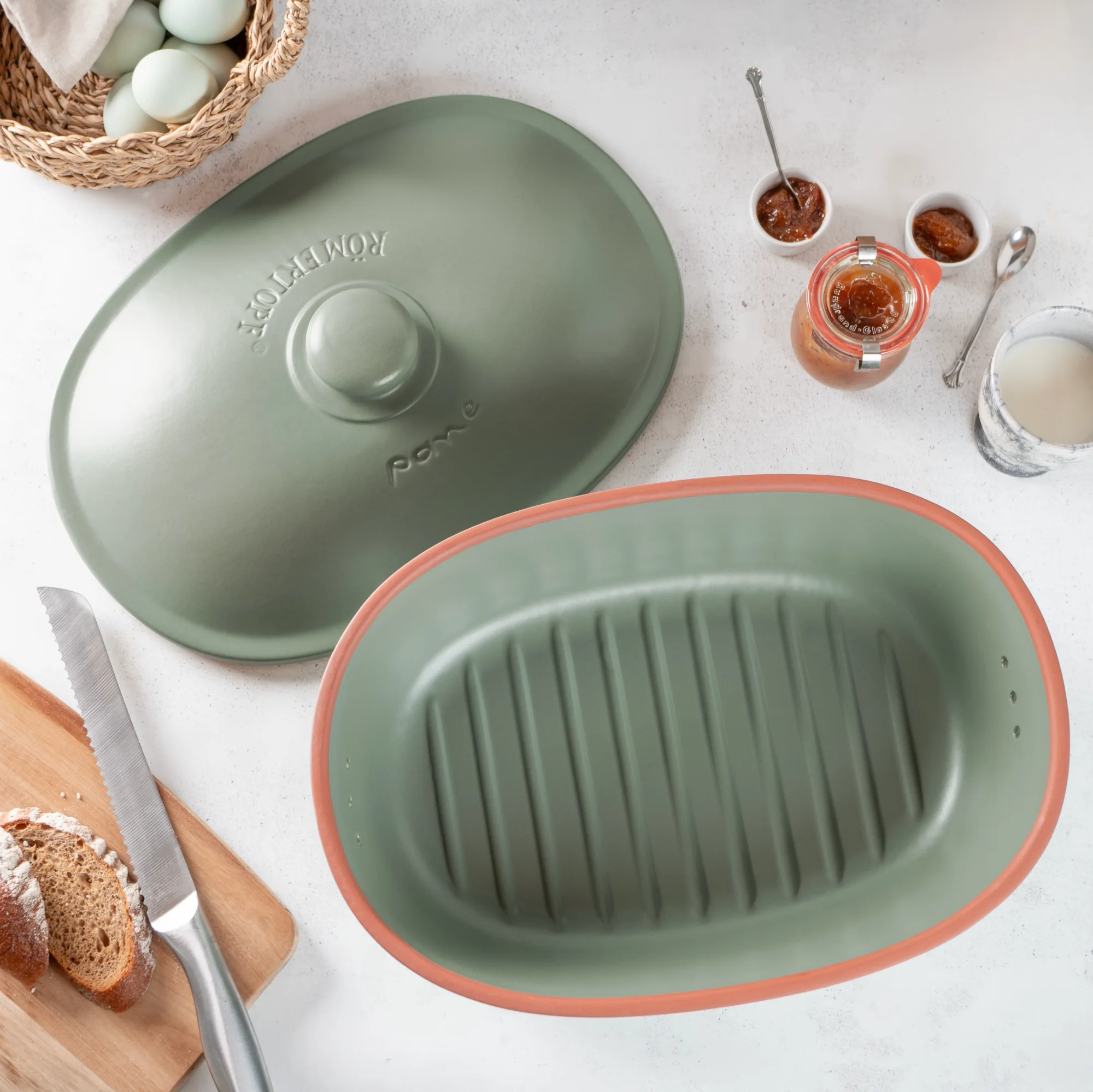 Römertopf Brottopf Maxi aus Keramik in Grün zur optimalen Brotaufbewahrung Grüner Brottopf aus Keramik mit Deckel, das Wort „Brot“ ist erhaben auf der Vorderseite eingeprägt; steht auf einem hellen Holztisch mit frischem Brot und Brotmesser daneben.