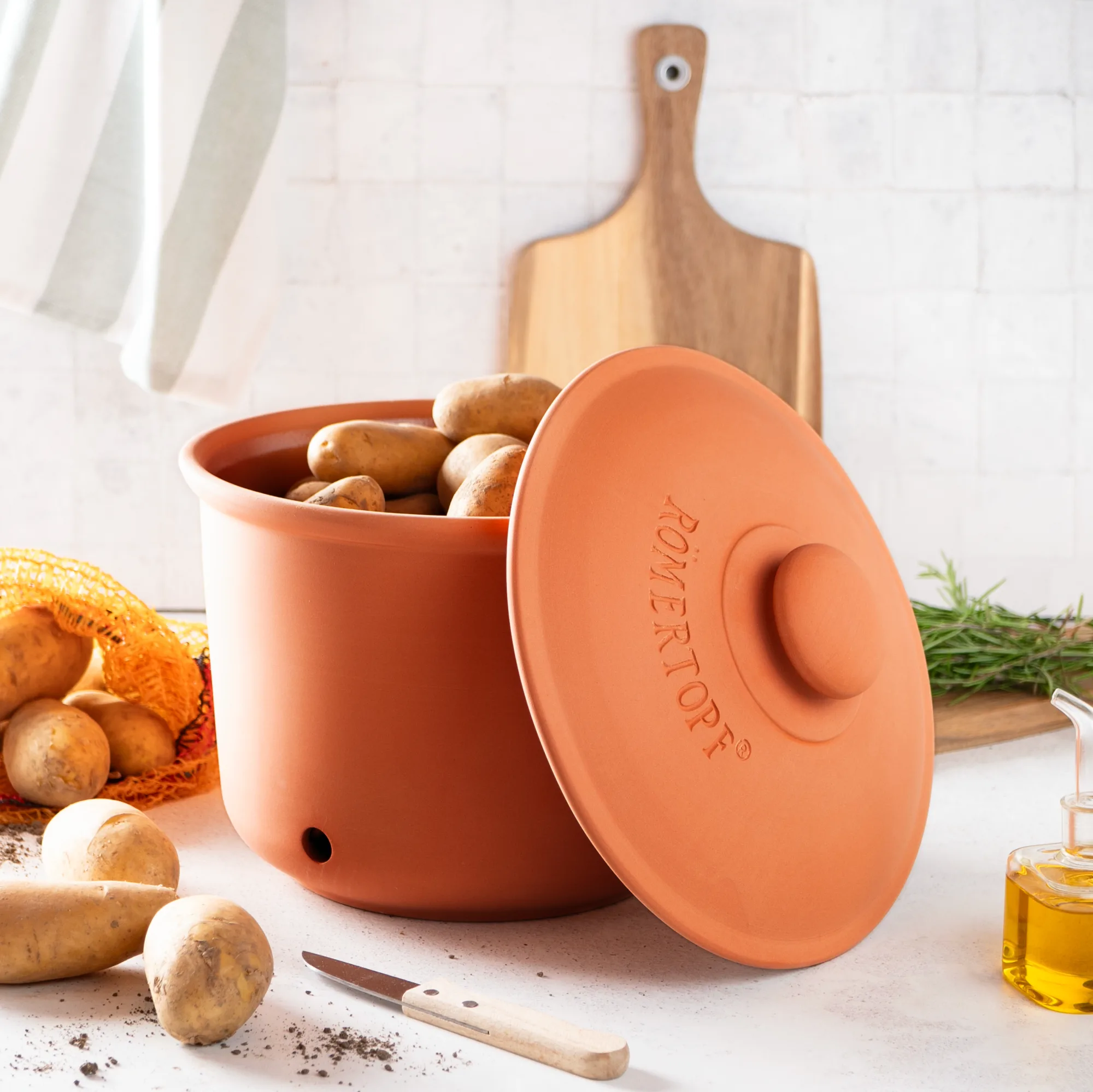 Römertopf Vorratstopf Set aus Terrakotta – 3-teiliges luftdichtes Keramik-Aufbewahrungsset für Küche Römertopf Vorratstopf-Set aus Terrakotta bestehend aus drei unterschiedlich großen Töpfen mit Deckeln, auf einem Holztisch mit Zwiebeln und Knoblauch dekoriert.