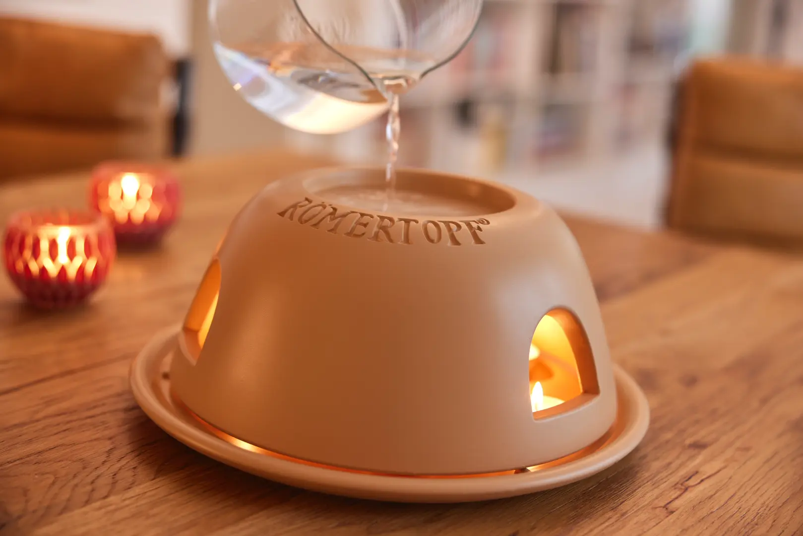 Römertopf Teelichtofen Heinz aus Keramik – energiesparender Mini-Ofen für gemütliche Wärme Römertopf Teelicht-Ofen Modell „Heinz“ aus naturfarbenem Ton mit rundem Deckel, steht auf weißem Untergrund; daneben drei Teelichter und ein Untersetzer.