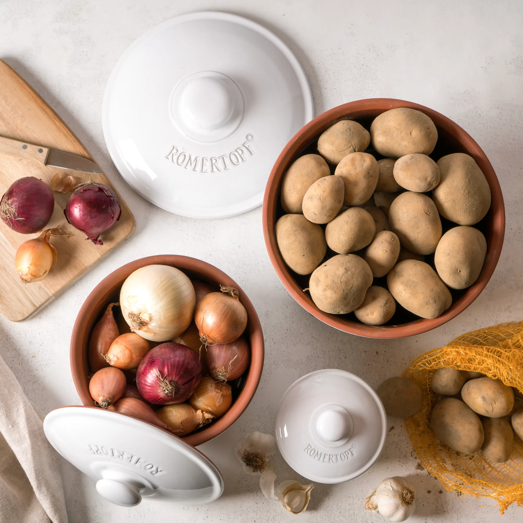 Römertopf Vorratstopf Set weiß – luftdichte Keramikbehälter zur Aufbewahrung von Lebensmitteln Römertopf Vorratstopf-Set aus weißer Keramik bestehend aus drei unterschiedlich großen Töpfen mit Deckeln, jeweils mit Beschriftung für Zwiebeln, Knoblauch und Kartoffeln sowie Belüftungsöffnungen zur Lagerung.