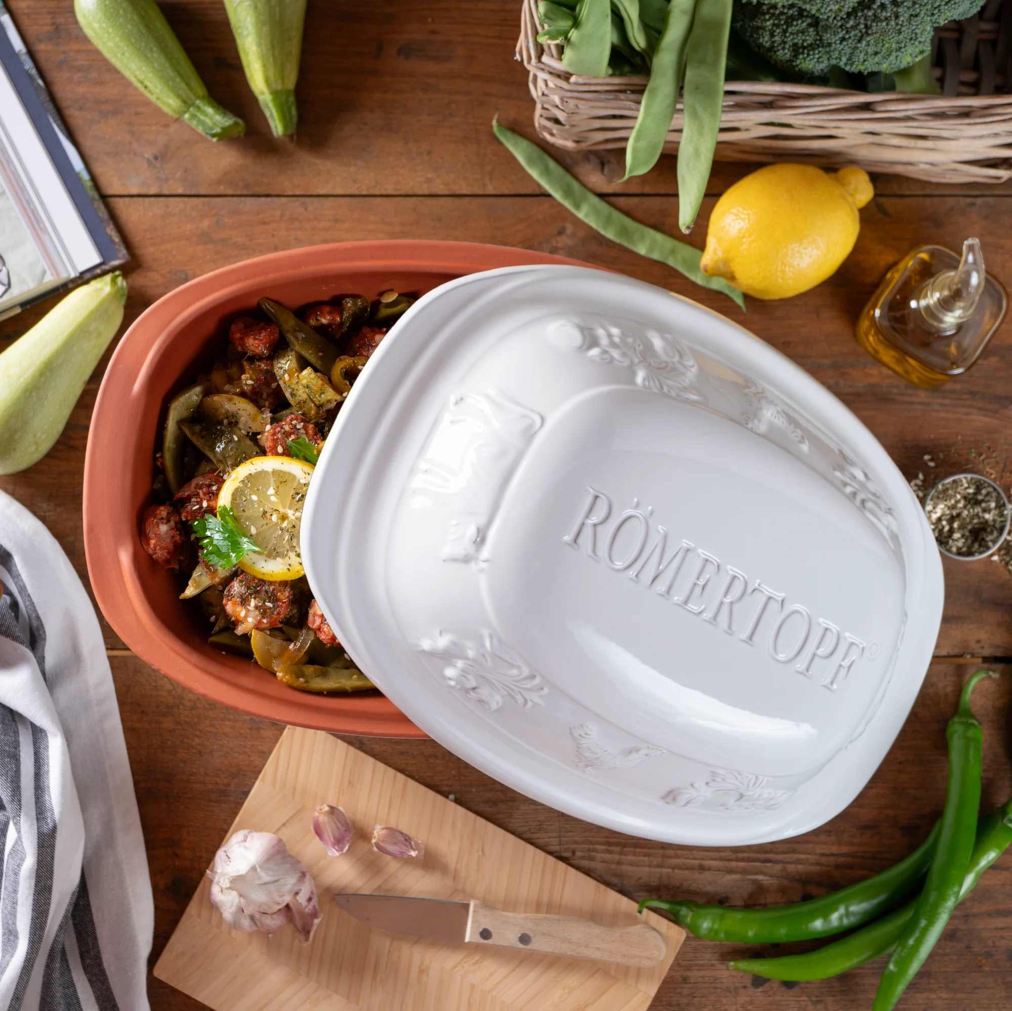 Römertopf Rustico Weiß für 4 Personen – Keramik Bräter oval mit Deckel Weißer Römertopf Rustico für 4 Personen mit Deckel, aus Keramik, auf hellem Untergrund stehend; Deckel zeigt geprägtes Muster, Topf mit zwei Henkeln seitlich.