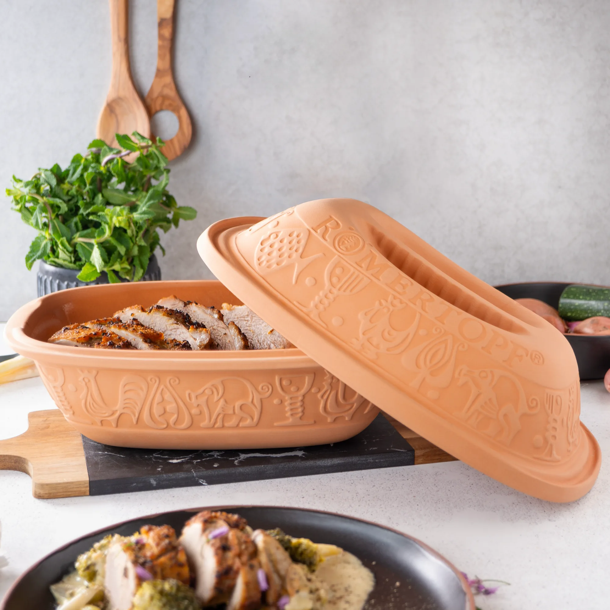 Klassischer Römertopf Bräter aus Naturton mit Deckel – Ideal zum fettfreien Garen Klassischer Römertopf-Bräter aus naturfarbenem Ton mit Deckel, ovaler Form und typischer Beschriftung, stehend auf weißem Untergrund.