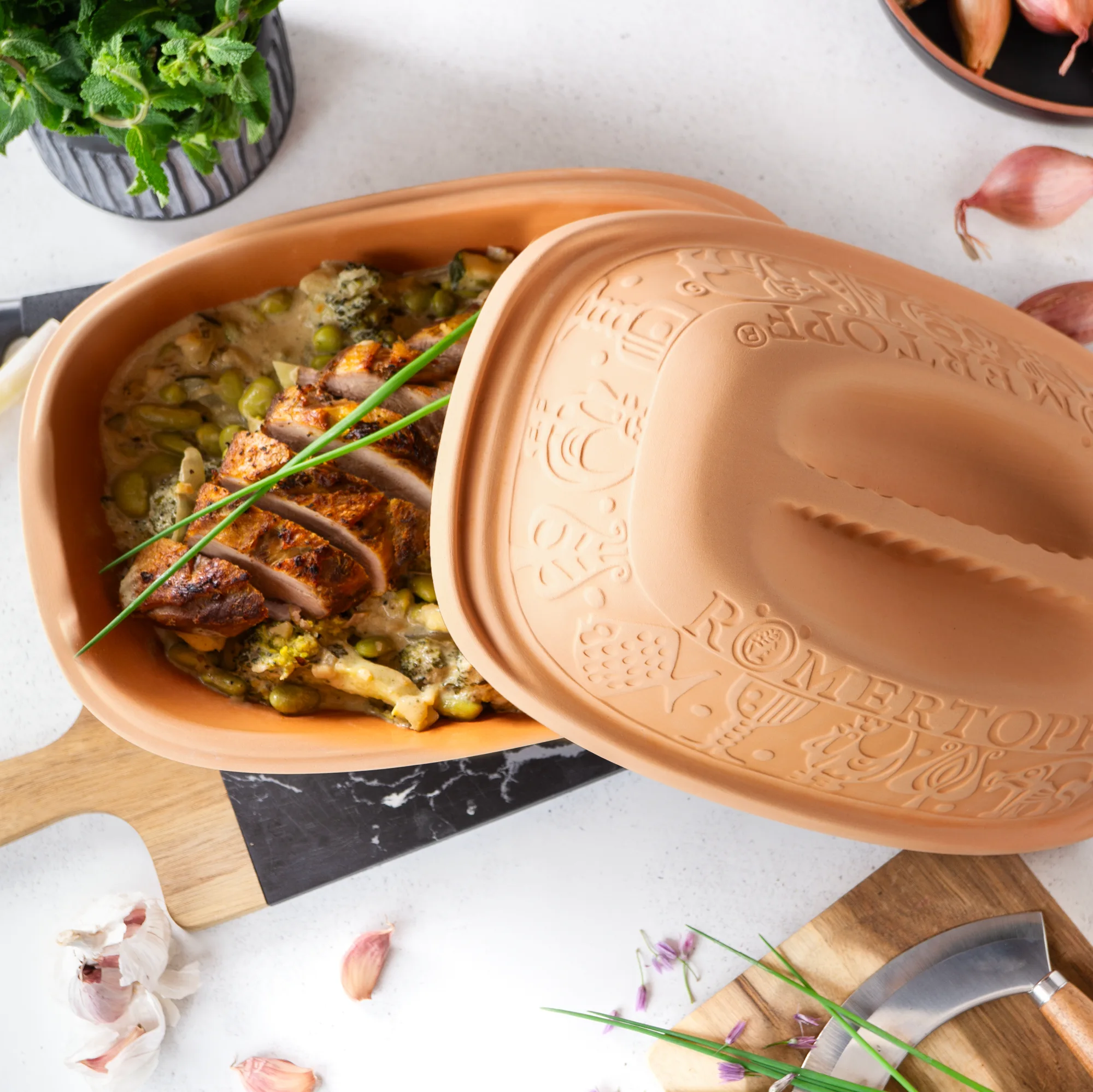 Klassischer Römertopf Bräter aus Naturton mit Deckel – Original RÖMERTOPF® für gesundes Garen Klassischer RÖMERTOPF Bräter aus rotem Ton mit passendem Deckel, ovaler Form, naturbelassene Oberfläche mit Prägung „RÖMERTOPF“ auf dem Deckel, auf weißem Hintergrund.