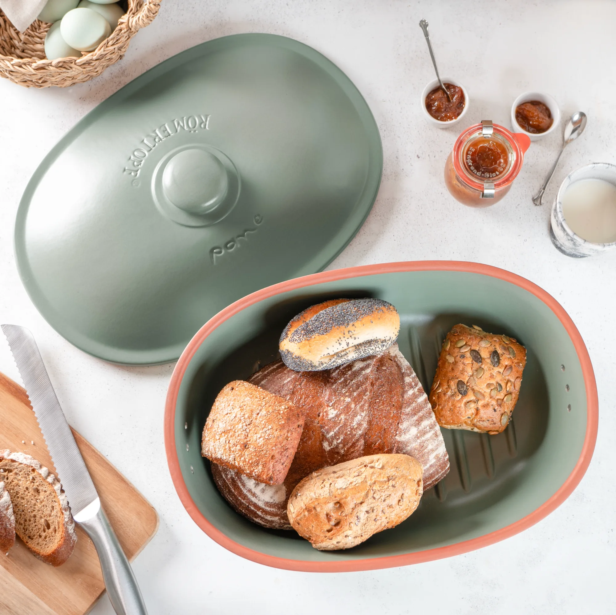 Brot-Frische-Topf Maxi Grün – Luftdichter Brottopf aus Keramik zur längeren Frischhaltung von Brot Grüner Römertopf Brot-Frische-Topf Maxi mit Deckel, auf einer hellen Oberfläche stehend; daneben ein angeschnittenes frisches Brot.