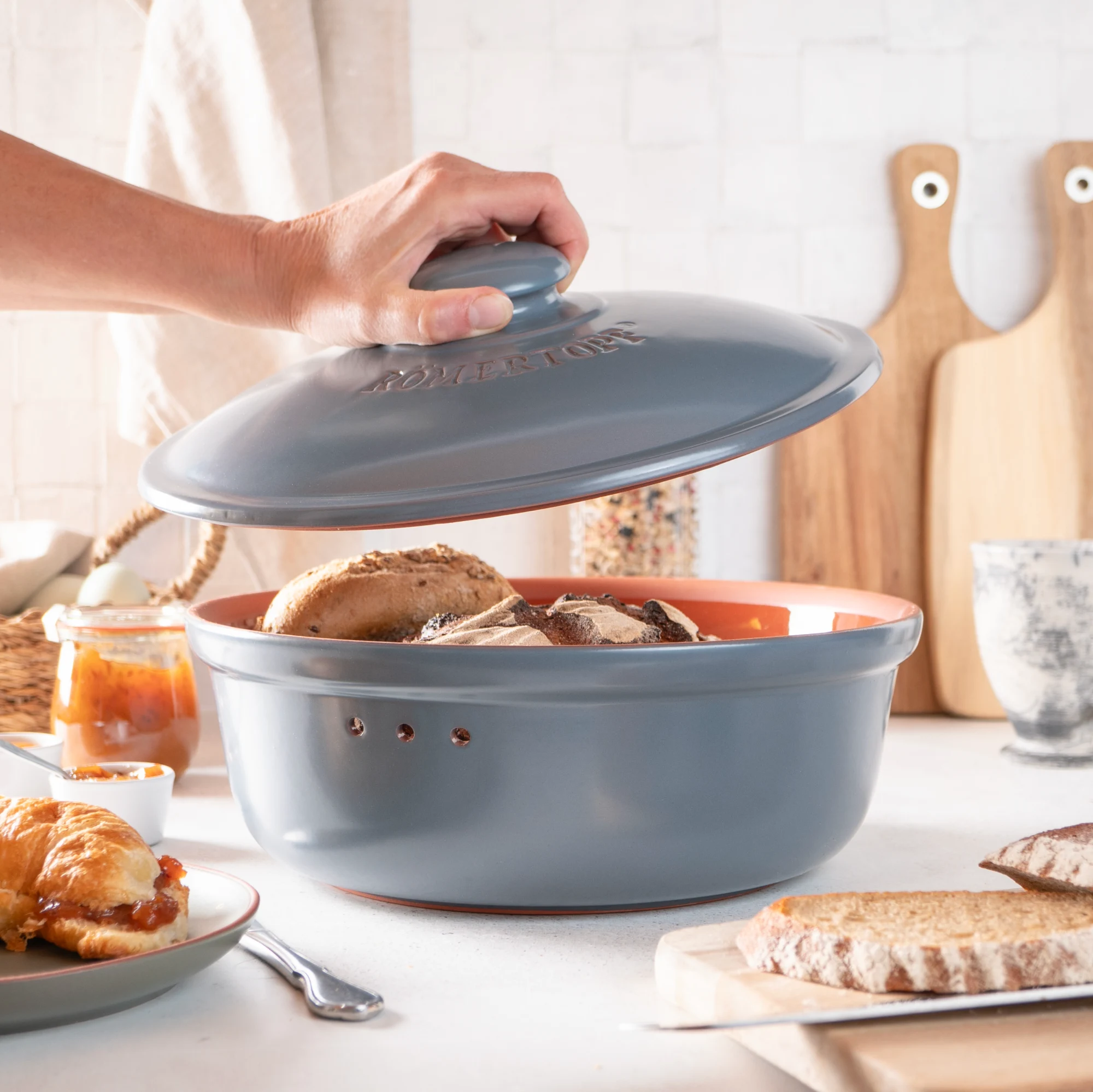 Römertopf Brottopf rund blaugrau – Frischetopf aus Naturton zur Brotaufbewahrung Runder Römertopf Brottopf in Blaugrau mit Deckel, seitlicher Griffkerbe und Aufschrift „RÖMERTOPF“ auf der Vorderseite, stehend auf hellem Untergrund.
