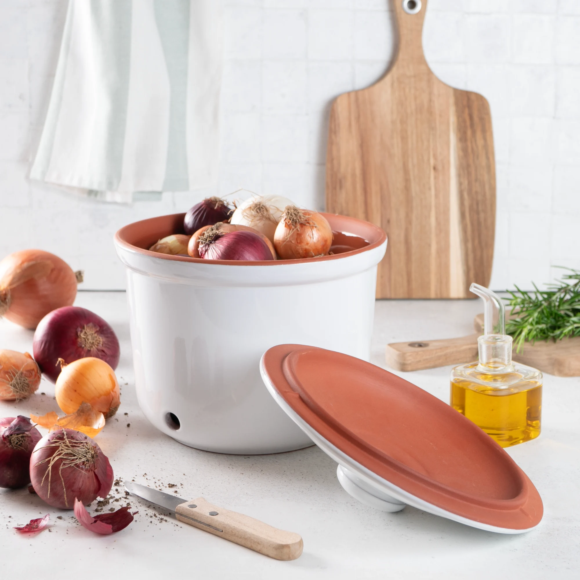 Römertopf Frischetopf Maxi Zwiebeltopf Weiß – Keramik Vorratsdose zur Zwiebelaufbewahrung Weißer Römertopf Frischetopf Maxi aus Keramik mit seitlichen Griffmulden, belüftetem Deckel und Lüftungslöchern, gefüllt mit roten und weißen Zwiebeln, auf heller Arbeitsfläche platziert.