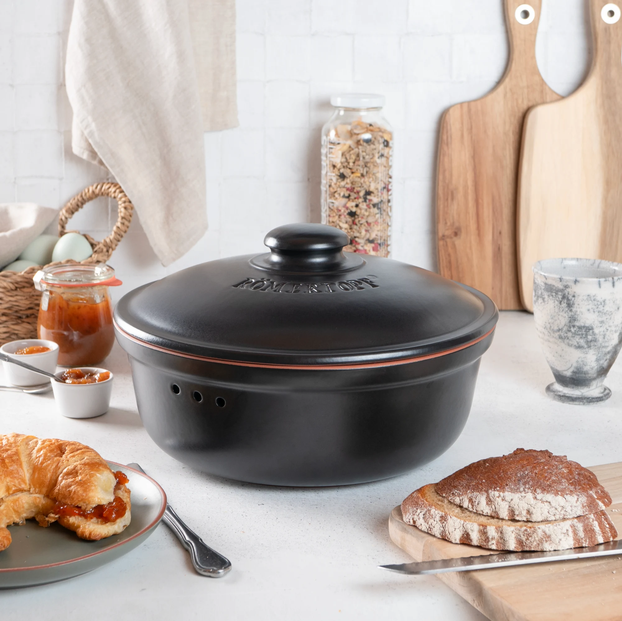 Römertopf Brottopf rund schwarz – Frischetopf aus Keramik zur Brotaufbewahrung Runder, schwarzer Römertopf Brottopf mit Deckel aus atmungsaktivem Keramikmaterial zur Aufbewahrung von Brot, auf weißem Hintergrund.