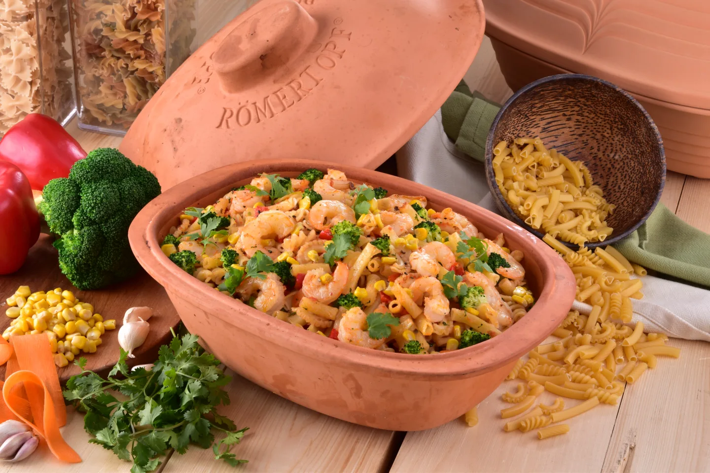 Römertopf Bräter Trend mit Gemüse und Fleisch – Rezeptidee für gesundes Garen im Tontopf Römertopf Bräter der Serie „Trend“ aus naturbelassener Keramik, befüllt mit Gemüse, Kräutern und Fleisch, bereit zum Garen im Ofen; dargestellt auf einem weißen Untergrund mit Zubehör im Hintergrund.