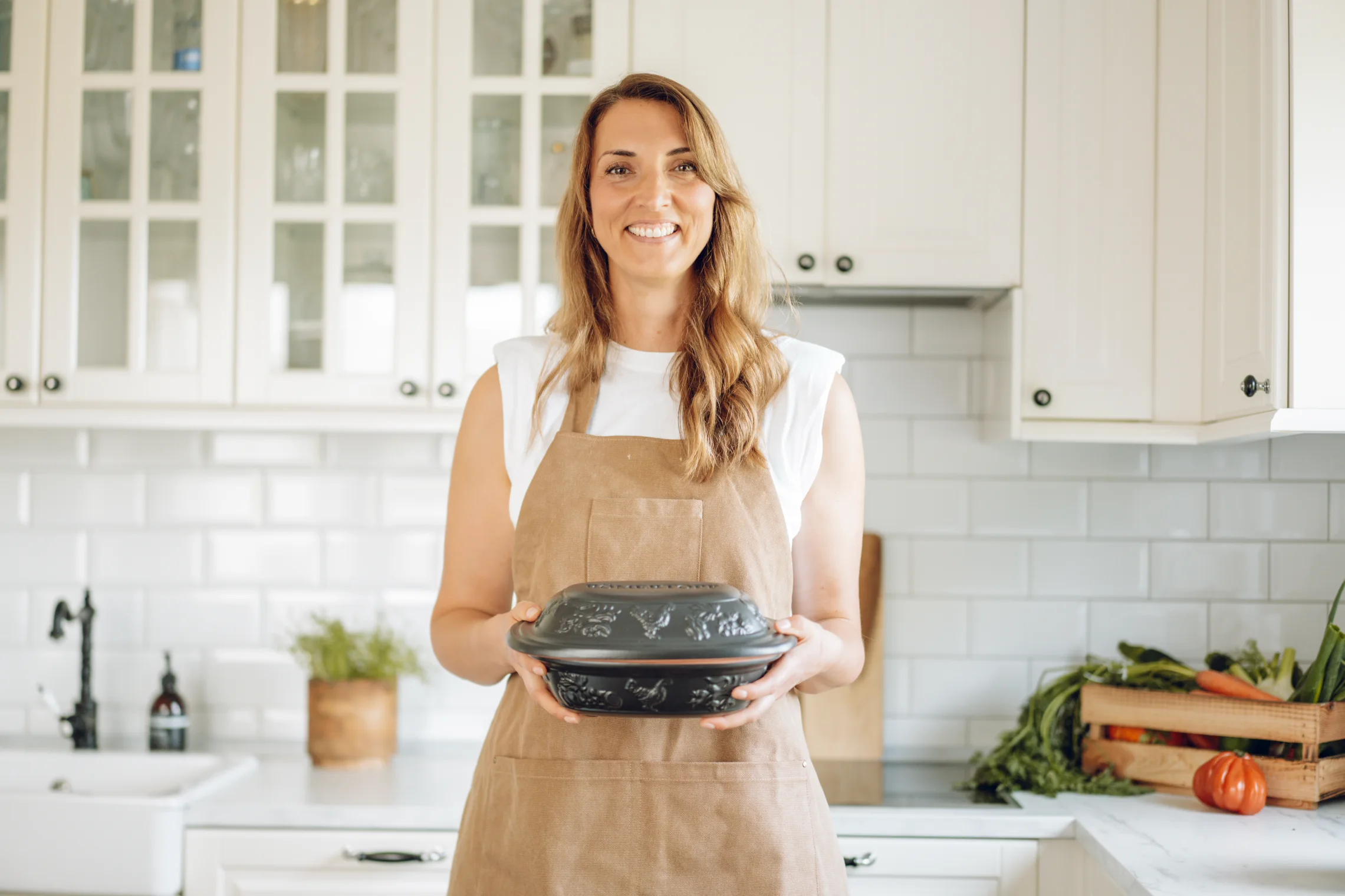 Römertopf Neuheiten 2024 – Innovative Keramik-Produkte für gesundes Kochen Vier verschiedene RÖMERTOPF-Keramikprodukte in dunklem Braun sind auf einem Holztisch arrangiert, darunter ein Bräter mit Deckel, eine Auflaufform, ein Brottopf und ein kleiner Behälter mit Holzlöffel; im Hintergrund ein heller Küchenbereich mit Pflanzen