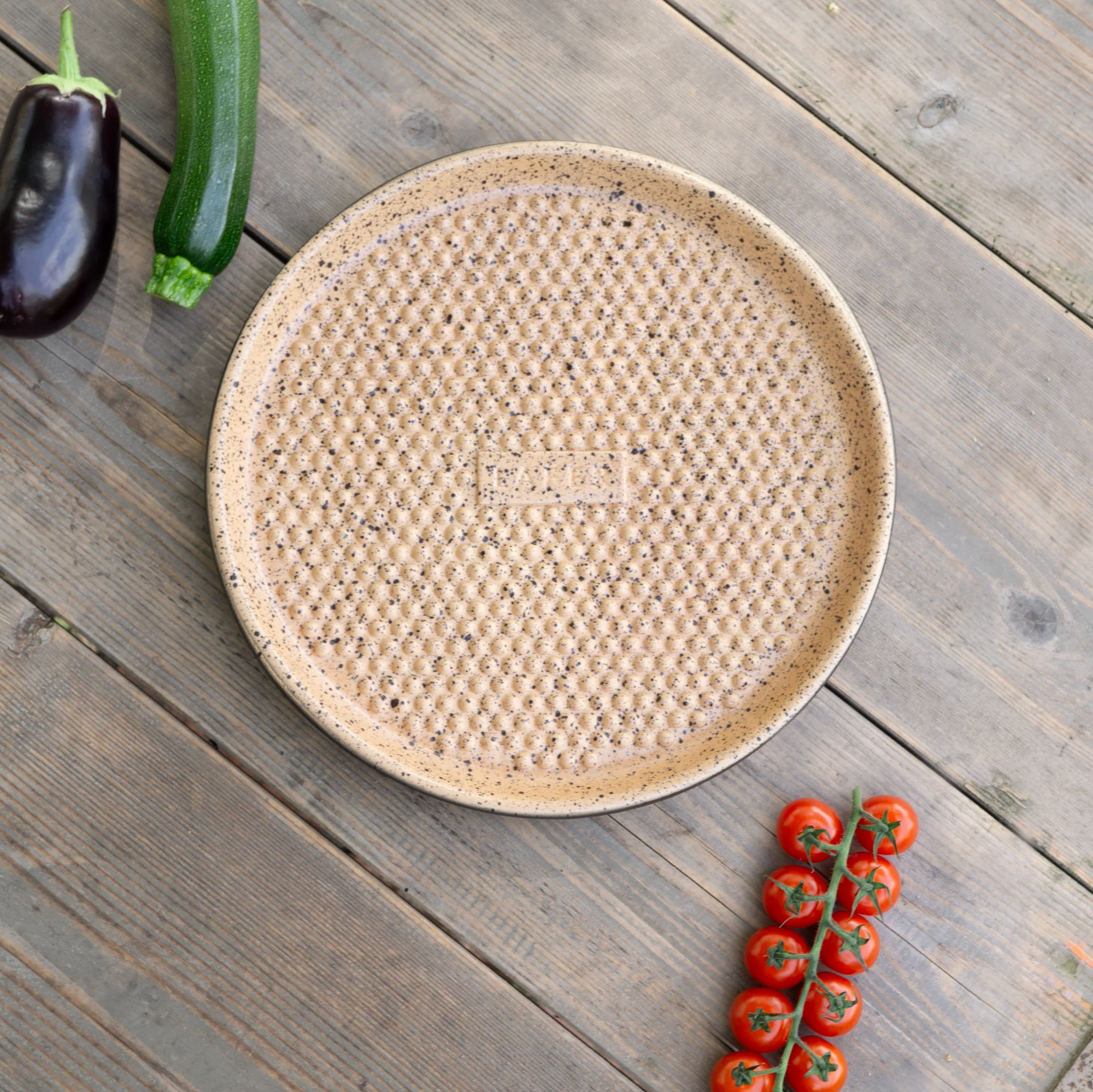 RÖMERTOPF Plancha rund mit Noppen – Grillplatte aus Naturton für schonendes Braten und Grillen Runde, schwarze Plancha-Grillplatte mit Noppenstruktur von Römertopf, aus Keramik, auf einem weißen Hintergrund liegend.