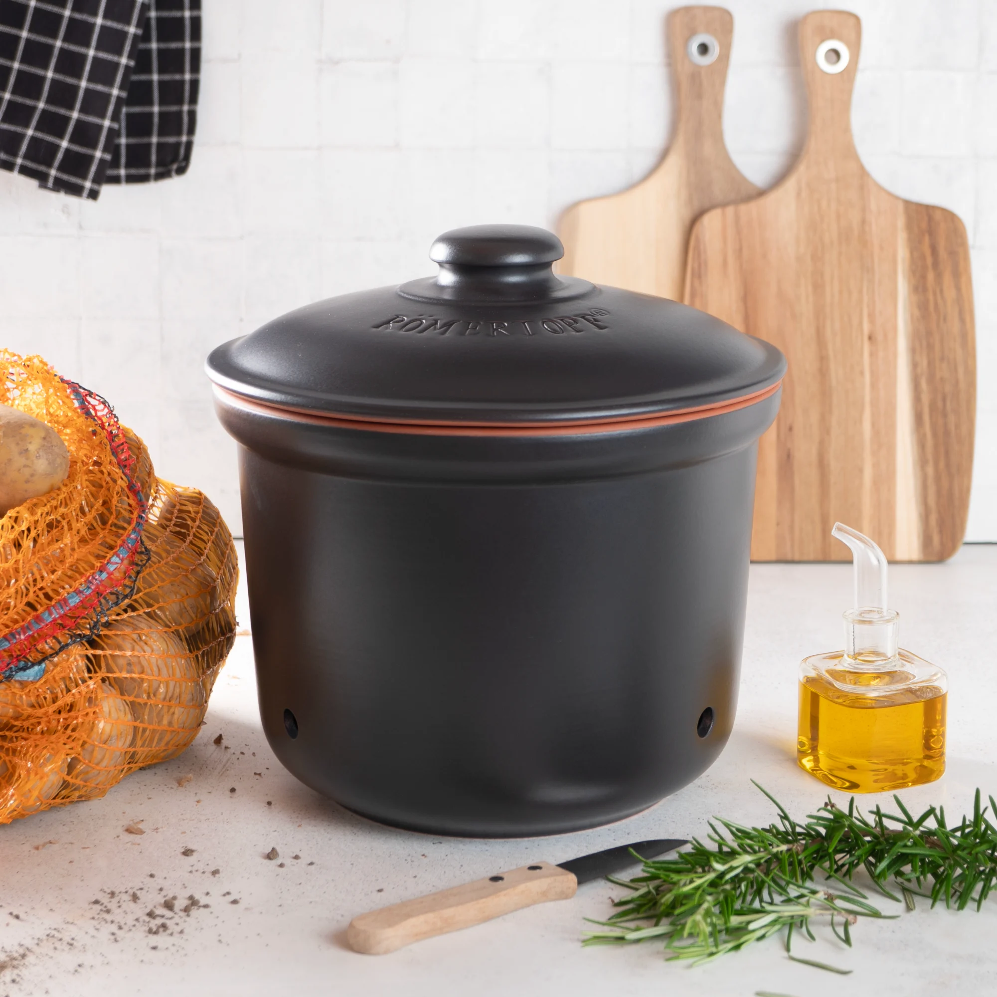 Römertopf Kartoffeltopf aus Keramik in Schwarz – Atmungsaktive Vorratsdose zur Aufbewahrung von Kartoffeln Schwarzer Römertopf-Kartoffeltopf mit Deckel, aus Keramik, seitlich belüftet, auf weißem Hintergrund.