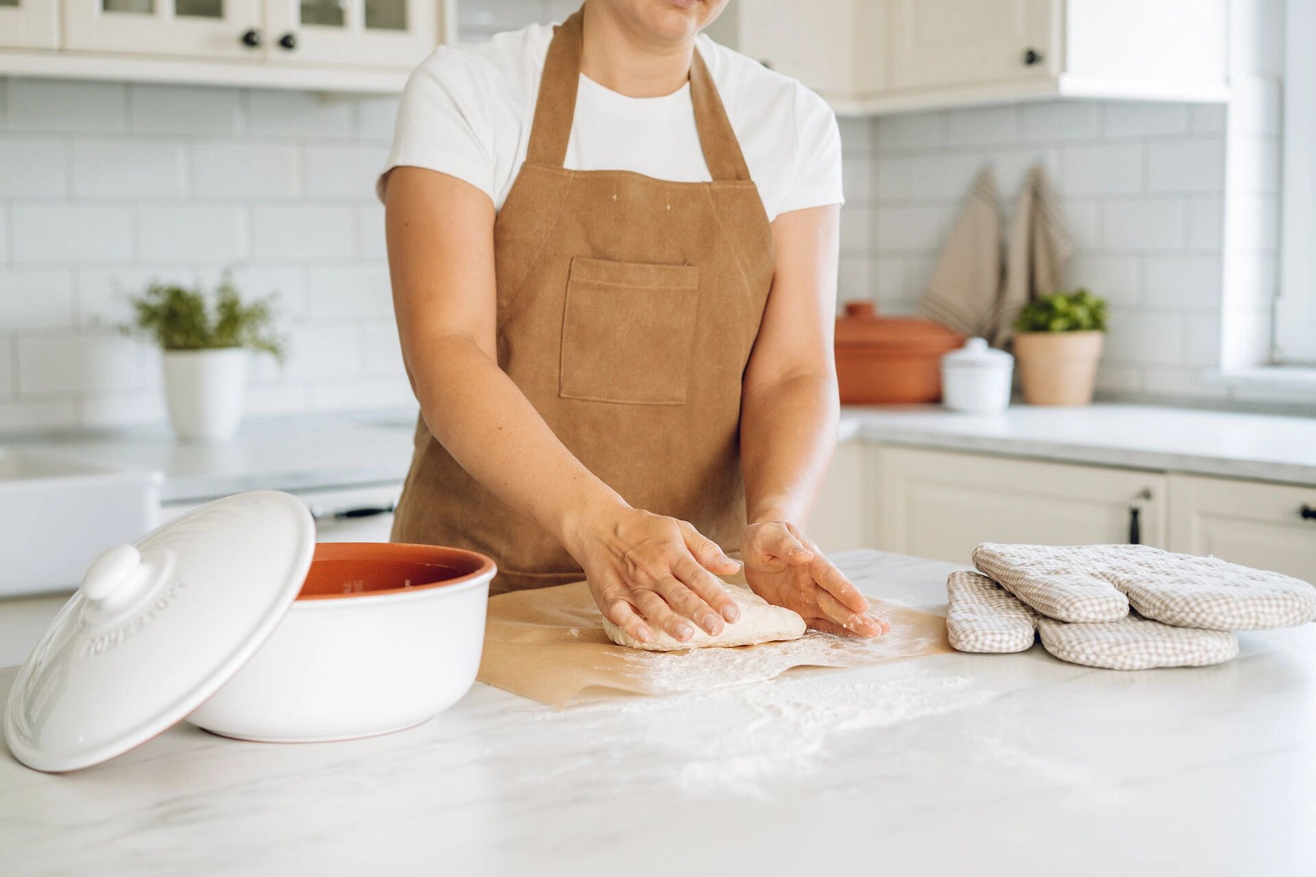 Frisch gebackenes Brot im traditionellen Römertopf aus Naturton Zwei gebackene Brotleibe liegen auf einem hölzernen Schneidebrett neben einem Römertopf aus Ton; im Hintergrund stehen Mehl, ein Schneebesen und ein Küchentuch auf einer Küchenarbeitsplatte.