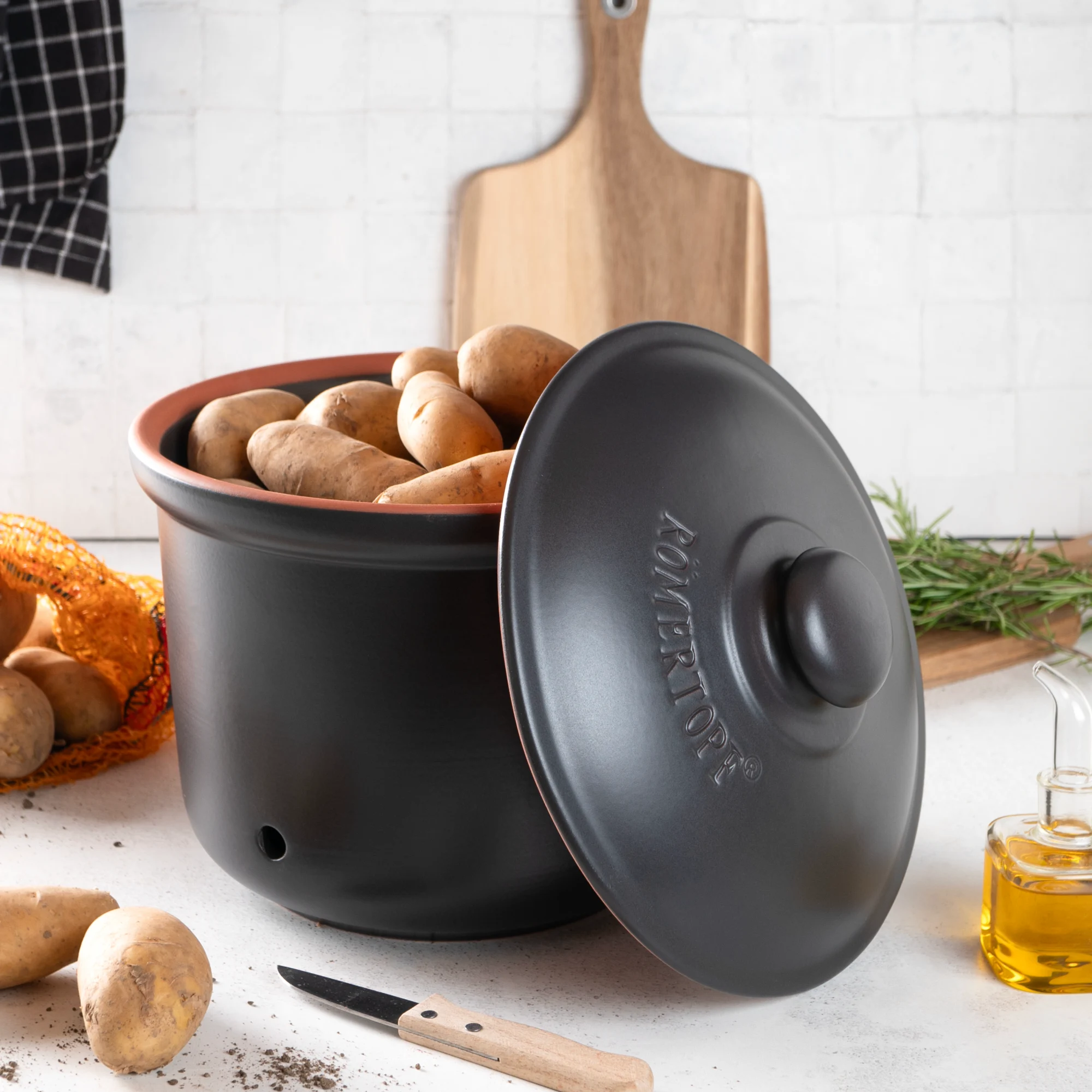 Römertopf Kartoffeltopf aus Keramik in Schwarz – ideal zur Lagerung von Kartoffeln Schwarzer Römertopf-Kartoffeltopf mit Deckel, seitlich belüftet, aus glasiertem Ton, auf hellem Hintergrund stehend.