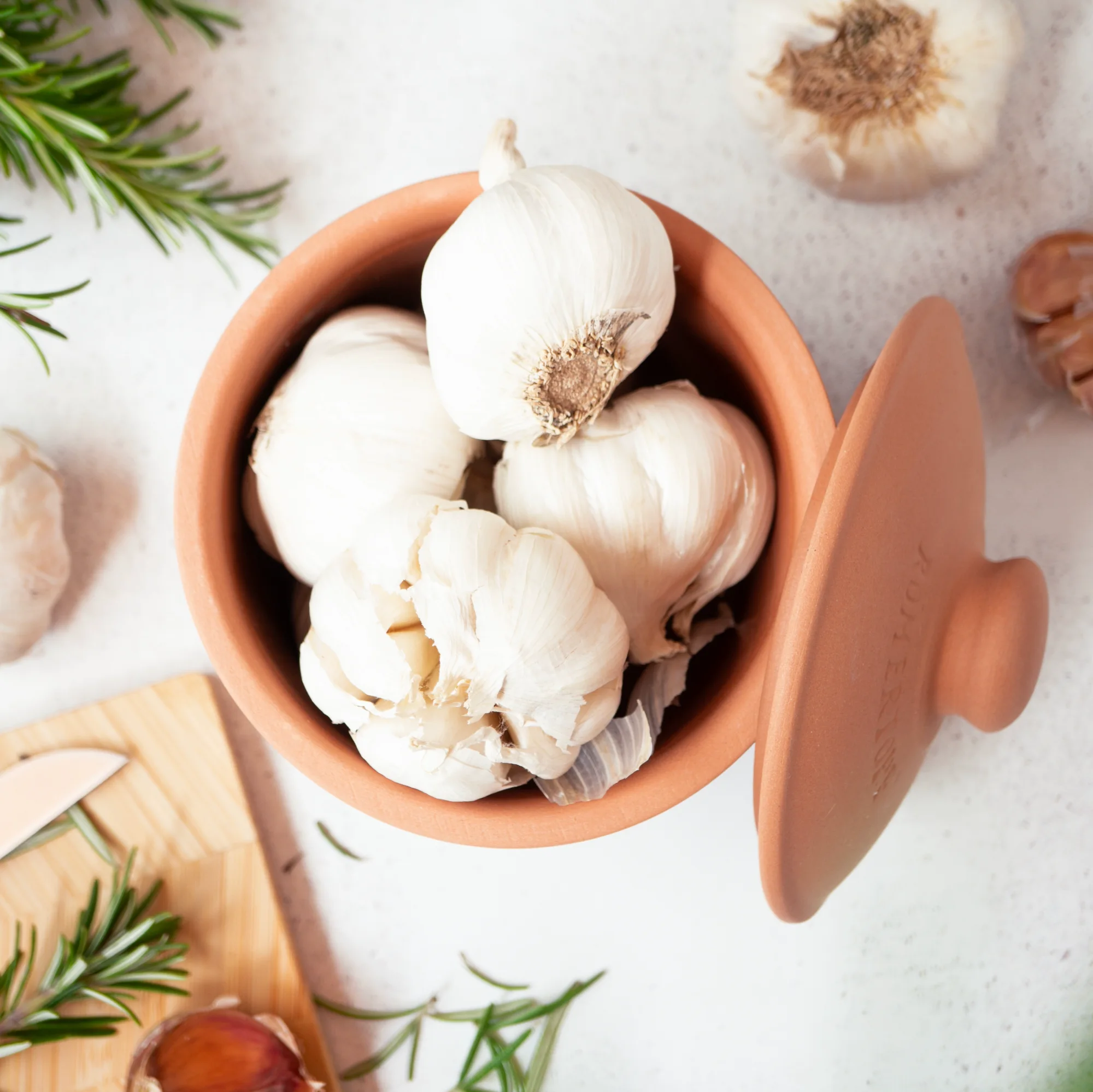 Römertopf Knoblauch-Frischetopf Mini aus Naturton – ideal zur Aroma- und Frischebewahrung Kleiner, cremefarbener Römertopf-Frischetopf mit seitlicher Aufschrift „RÖMERTOPF“ und Deckel, daneben eine aufgeschnittene Knoblauchknolle auf weißem Hintergrund.