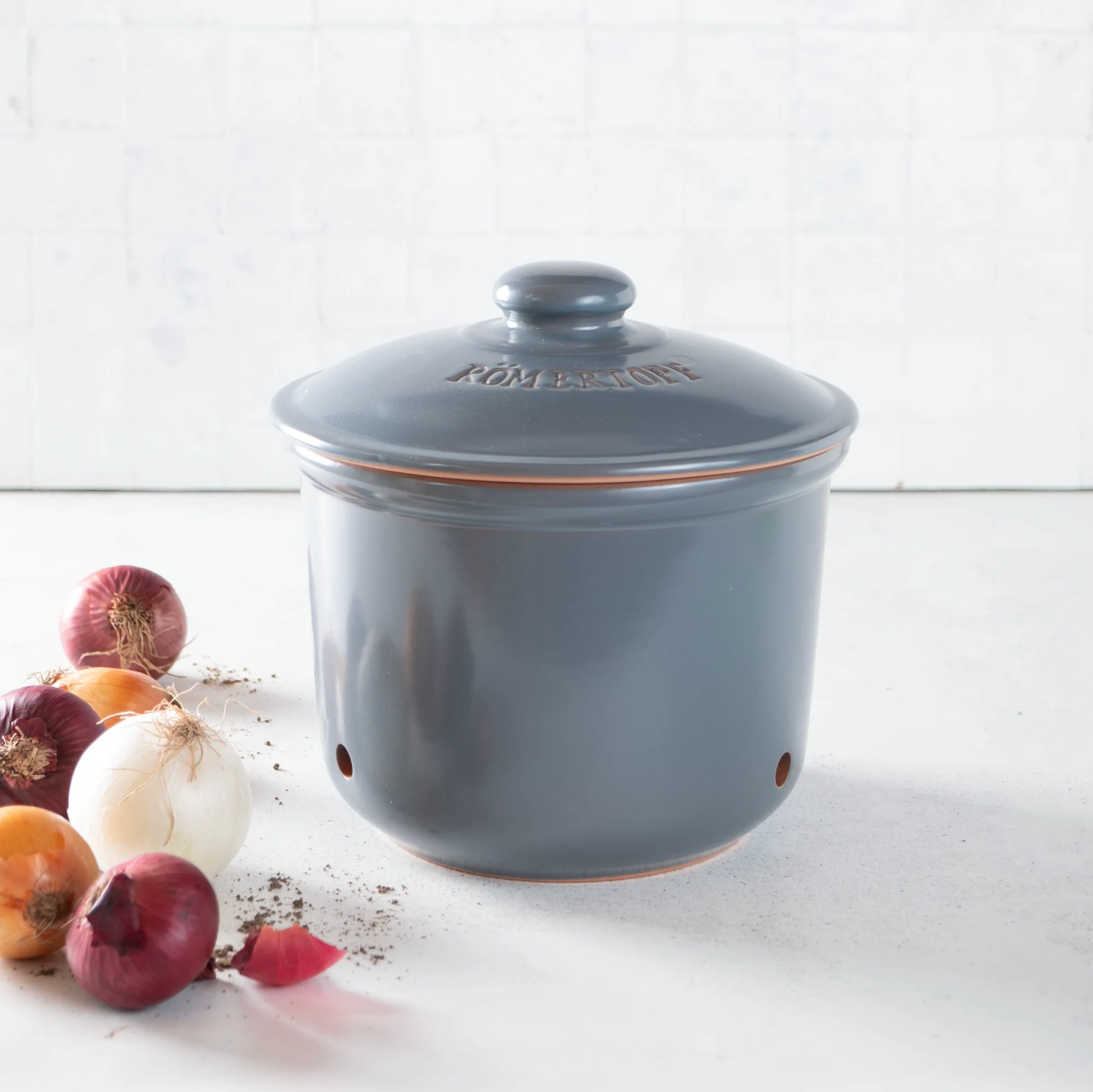 RÖMERTOPF Zwiebeltopf Maxi Blaugrau – Frischetopf zur Zwiebelaufbewahrung aus Naturton Blaugrauer Römertopf Frischetopf Maxi aus Keramik mit Deckel, belüftet durch kleine Löcher, geeignet zur Aufbewahrung von Zwiebeln, abgebildet auf weißem Hintergrund.
