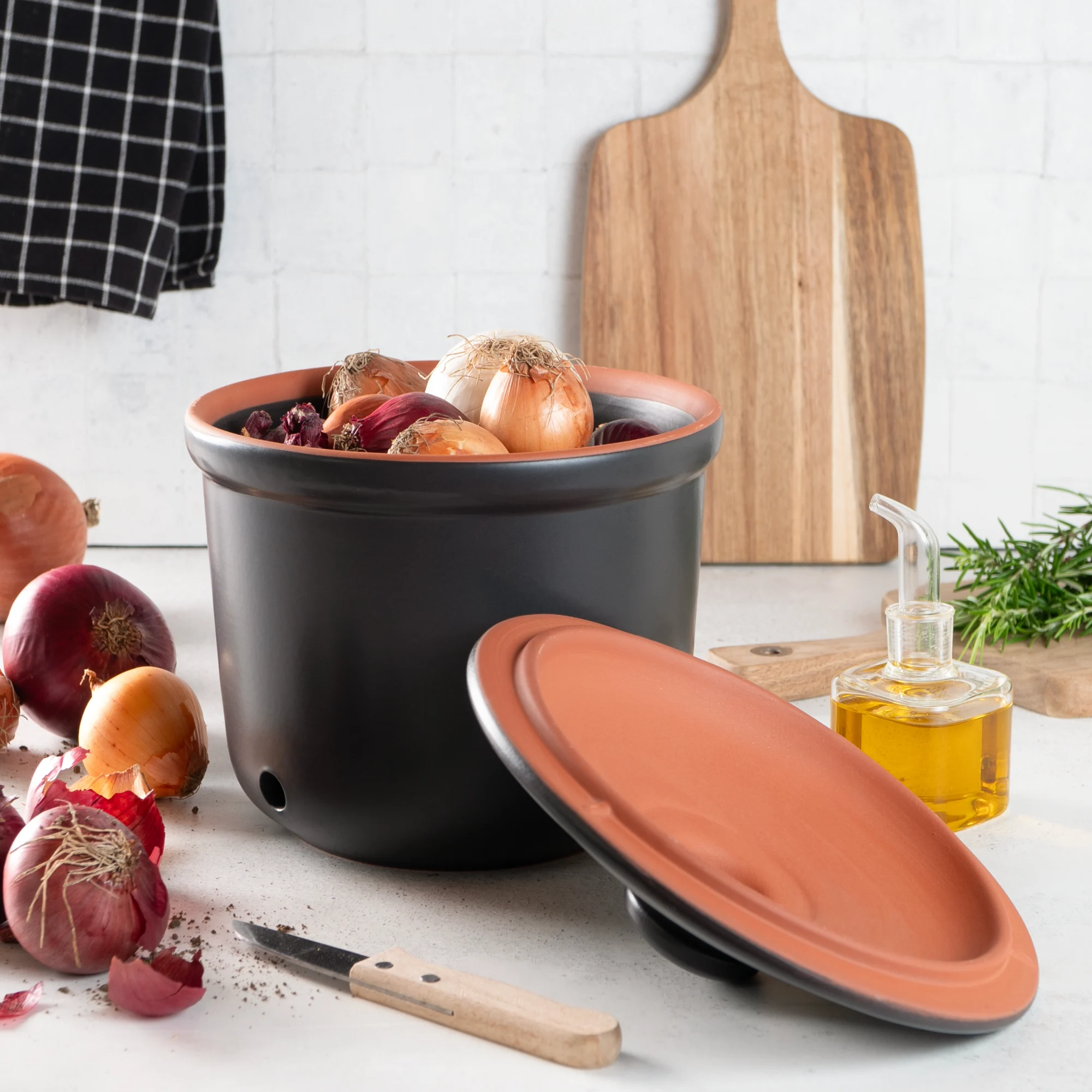 Römertopf Zwiebeltopf Maxi Schwarz – Atmungsaktiver Frischetopf zur optimalen Lagerung von Zwiebeln Schwarzer Römertopf-Frischetopf aus Keramik in Maxi-Größe mit Deckel und seitlichen Luftlöchern, gefüllt mit Zwiebeln, auf einem hellen Untergrund.
