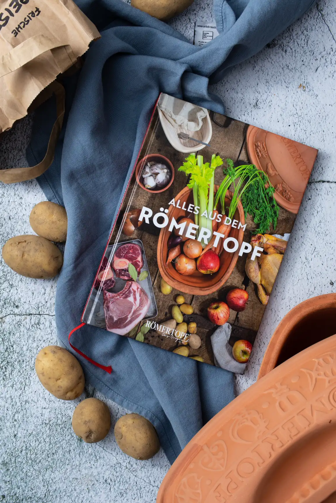 Saftiges Ofenhähnchen mit Gemüse im klassischen Römertopf zubereitet Zubereitetes Gericht in einem offenen Römertopf: goldbraunes Brathähnchen auf Gemüse wie Karotten, Sellerie und Zwiebeln, angerichtet in einer rechteckigen, naturfarbenen Tonform auf einem hellen Untergrund.