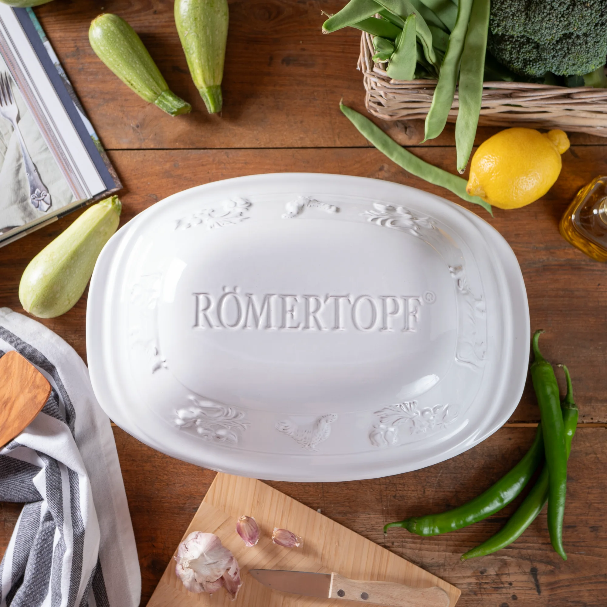 Römertopf Rustico Weiß für 4 Personen – ovaler Schmortopf mit Deckel aus Naturton Weißer Römertopf aus der Serie "Rustico" für vier Personen, oval geformt mit strukturiertem Deckel, auf weißem Hintergrund.