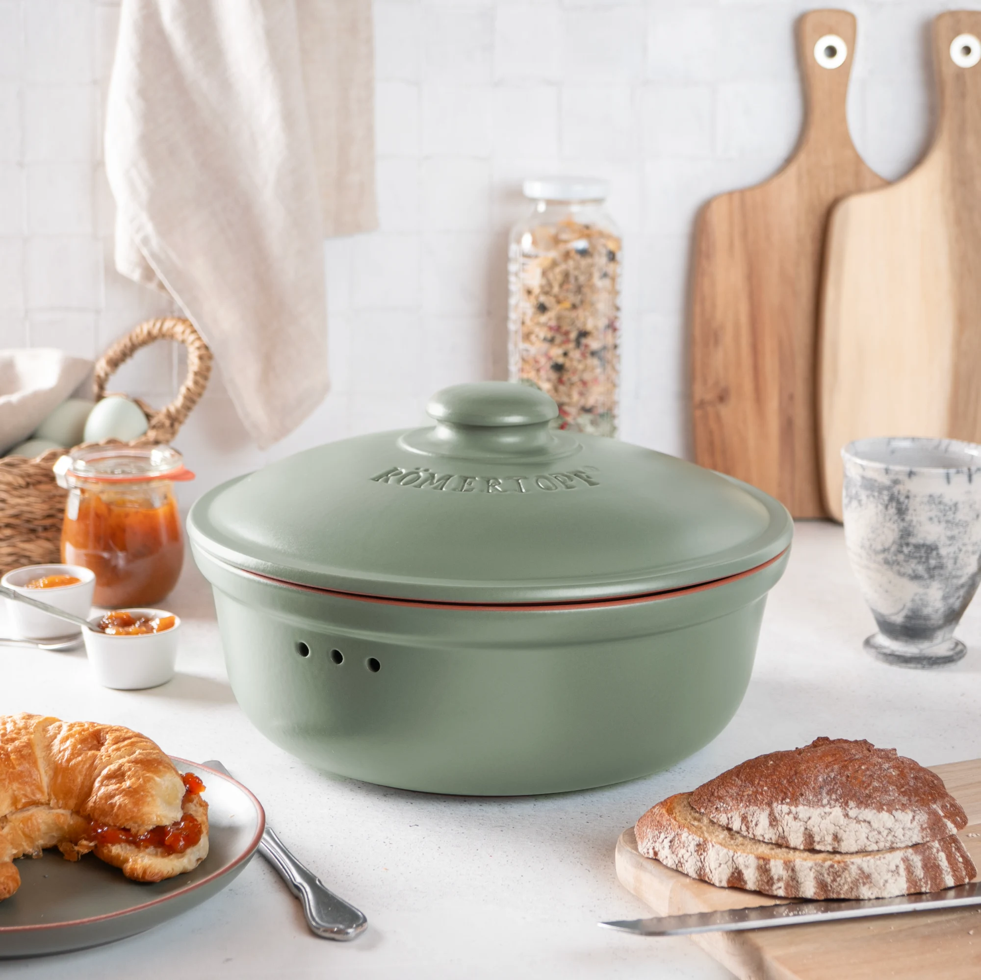 Römertopf Brottopf rund grün – Frischetopf aus Naturton zur Aufbewahrung von Brot und Brötchen Runder Römer Brottopf in Grün mit Deckel, aus Keramik gefertigt, auf weißem Hintergrund stehend.