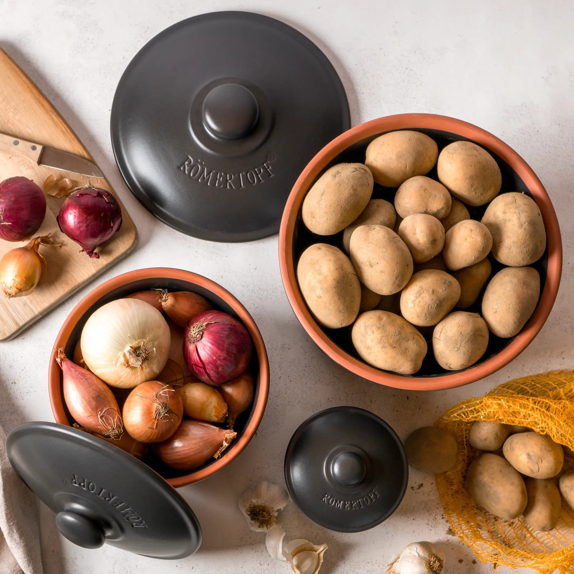 Römertopf Vorratstopf Set Schwarz – 3-teiliges Keramik-Set zur luftdichten Aufbewahrung von Lebensmitteln Zweiteiliges Vorratstopf-Set aus schwarzer Keramik von Römertopf mit Holzdeckeln, auf hellgrauem Untergrund stehend; ein Topf ist größer und der andere kleiner, beide mit Römertopf-Logo.