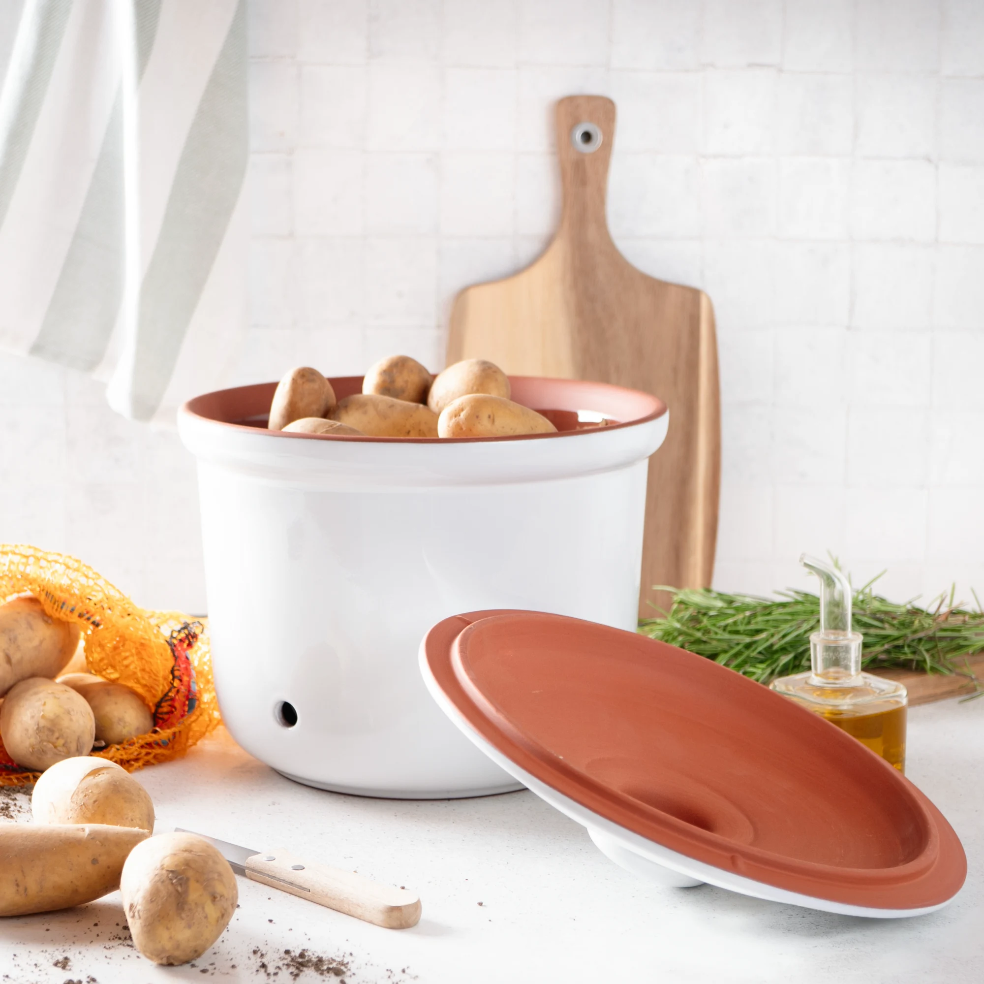 RÖMERTOPF Kartoffeltopf Maxi Plus weiß – Großer atmungsaktiver Tontopf zur Lagerung von Kartoffeln Weiß glasierter Römertopf-Kartoffeltopf mit Deckel, Modell Maxi Plus, auf neutralem Hintergrund; daneben liegen rohe Kartoffeln zur Veranschaulichung der Verwendung.