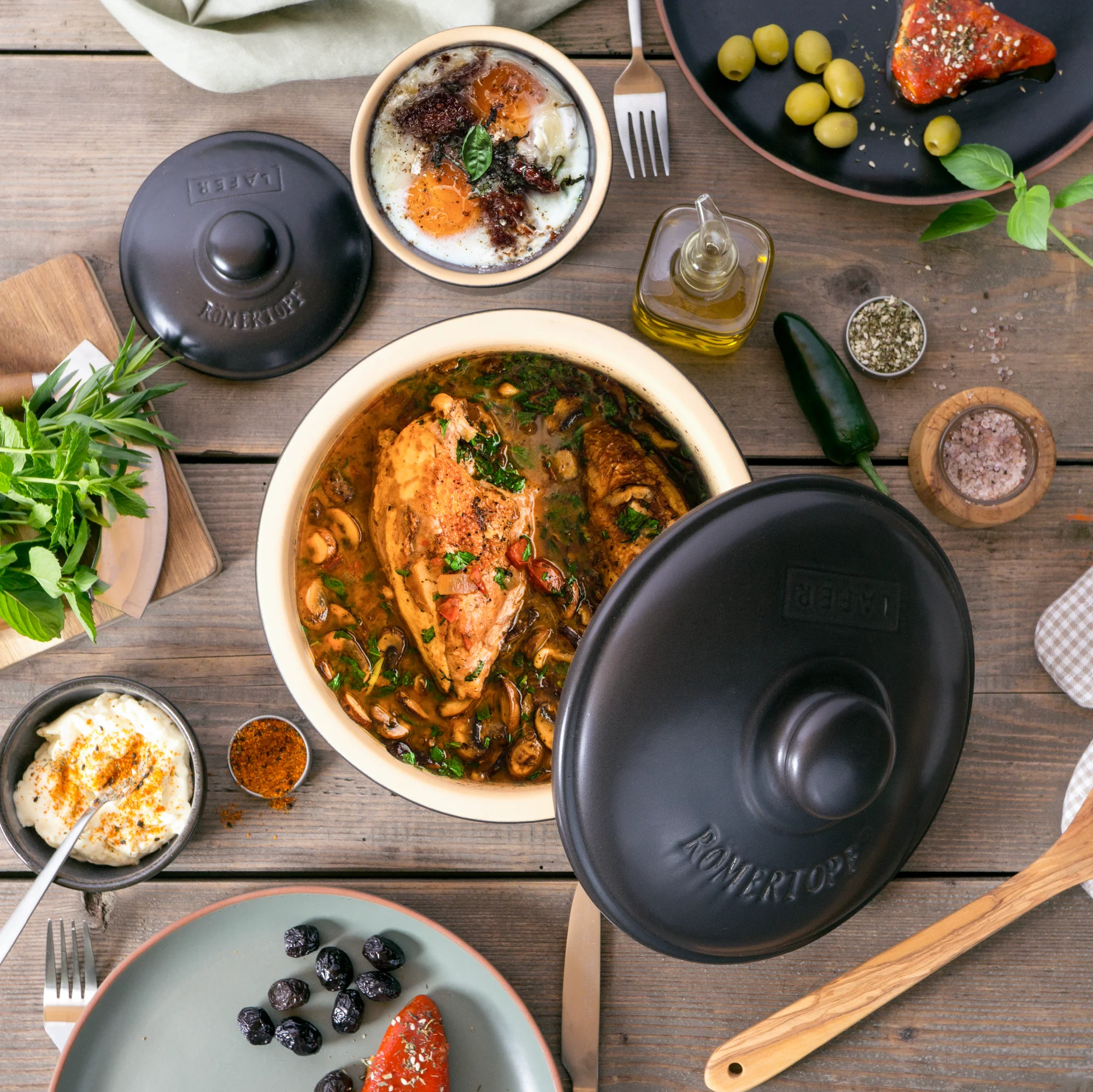 RÖMERTOPF BBQ Schmortopf aus Ton mit Deckel – Grill- und Backofentopf für saftige Schmorgerichte Rechteckiger Römertopf BBQ-Schmortopf aus rotem Ton mit passendem Deckel, auf einem Holztisch im Freien platziert; im Hintergrund unscharf Grillzubehör und grüne Pflanzen erkennbar.