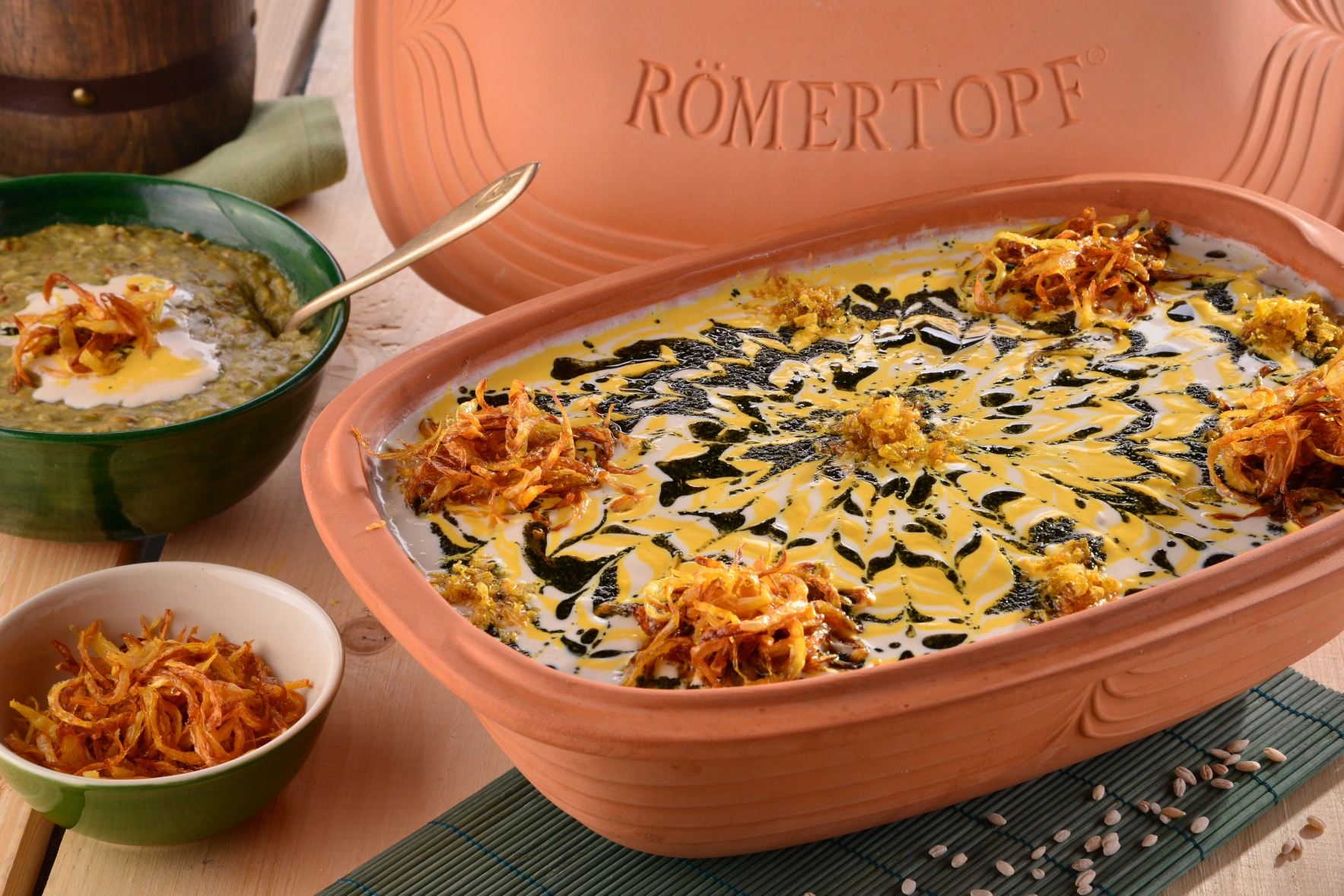 Moderner Römertopf Bräter mit leckerem Gemüsegericht auf dunklem Untergrund Ein gefüllter Römertopf-Topf mit Fleisch, Kräutern, Zwiebeln und Gemüse auf einem gedeckten Holztisch – daneben ein Servierteller mit Bratenstücken, Besteck und frischen Kräutern, im modernen Küchenambiente.