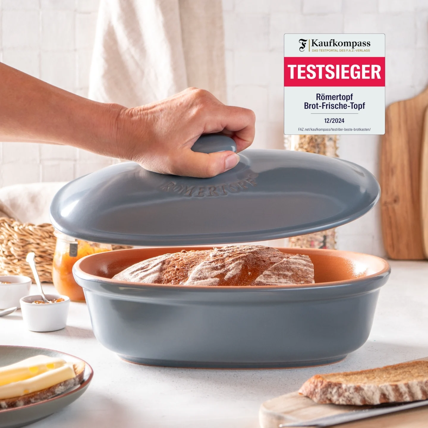 Römertopf Brottopf Medi Blaugrau – Keramik Frischetopf zur Brotaufbewahrung Römertopf Brottopf aus Keramik in blaugrauem Farbton, oval geformt mit Deckel, Belüftungslöchern an den Seiten und „Römertopf“-Prägung auf der Vorderseite, stehend auf heller Unterlage vor neutralem Hintergrund.