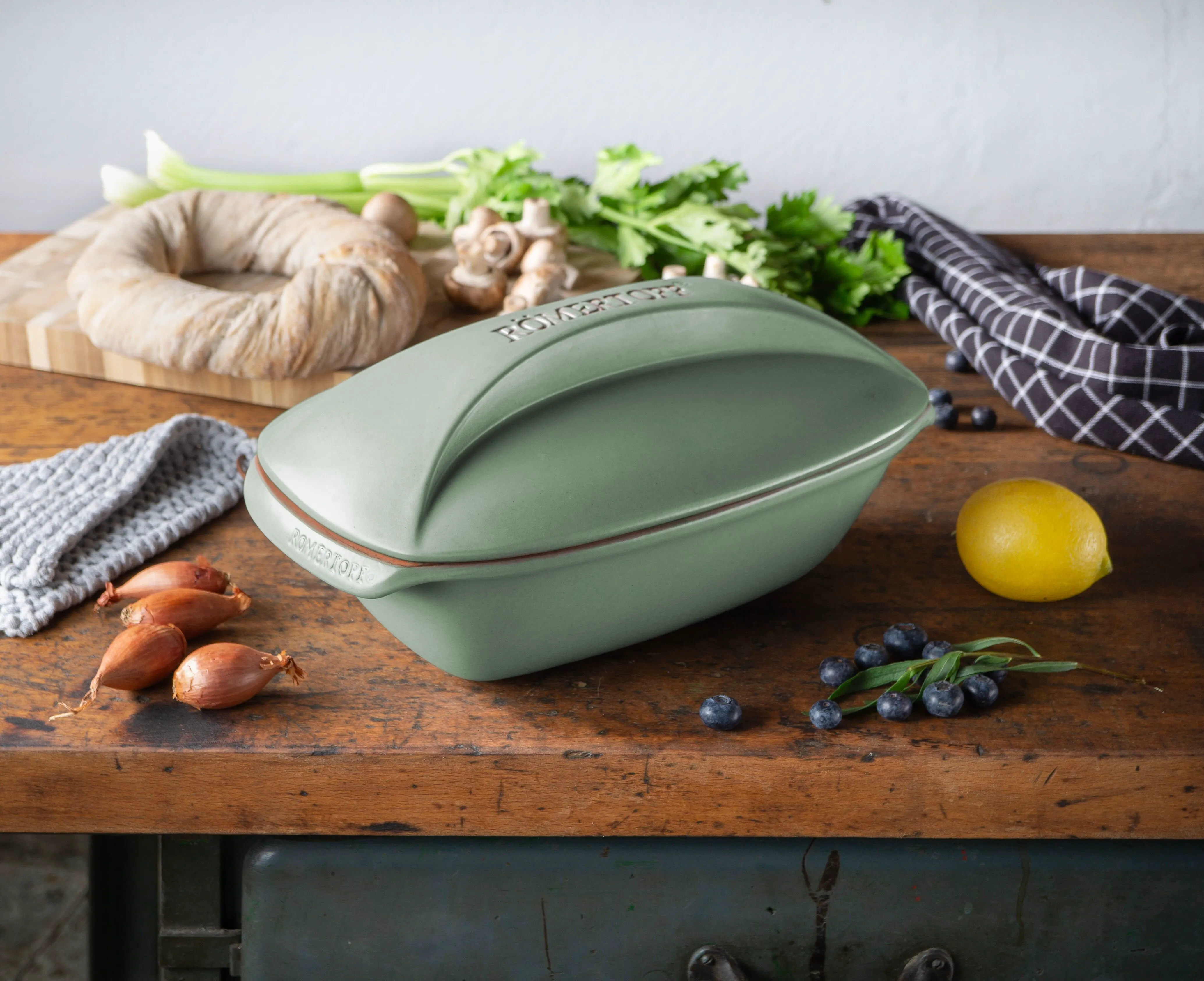 Römertopf in neuen Farben – nachhaltiges Kochen mit stilvollem Design Drei Römertopf-Bräter in den Farben Dunkelblau, Grün und Hellgrau stehen nebeneinander auf einem Holztisch vor einem hellen Hintergrund.