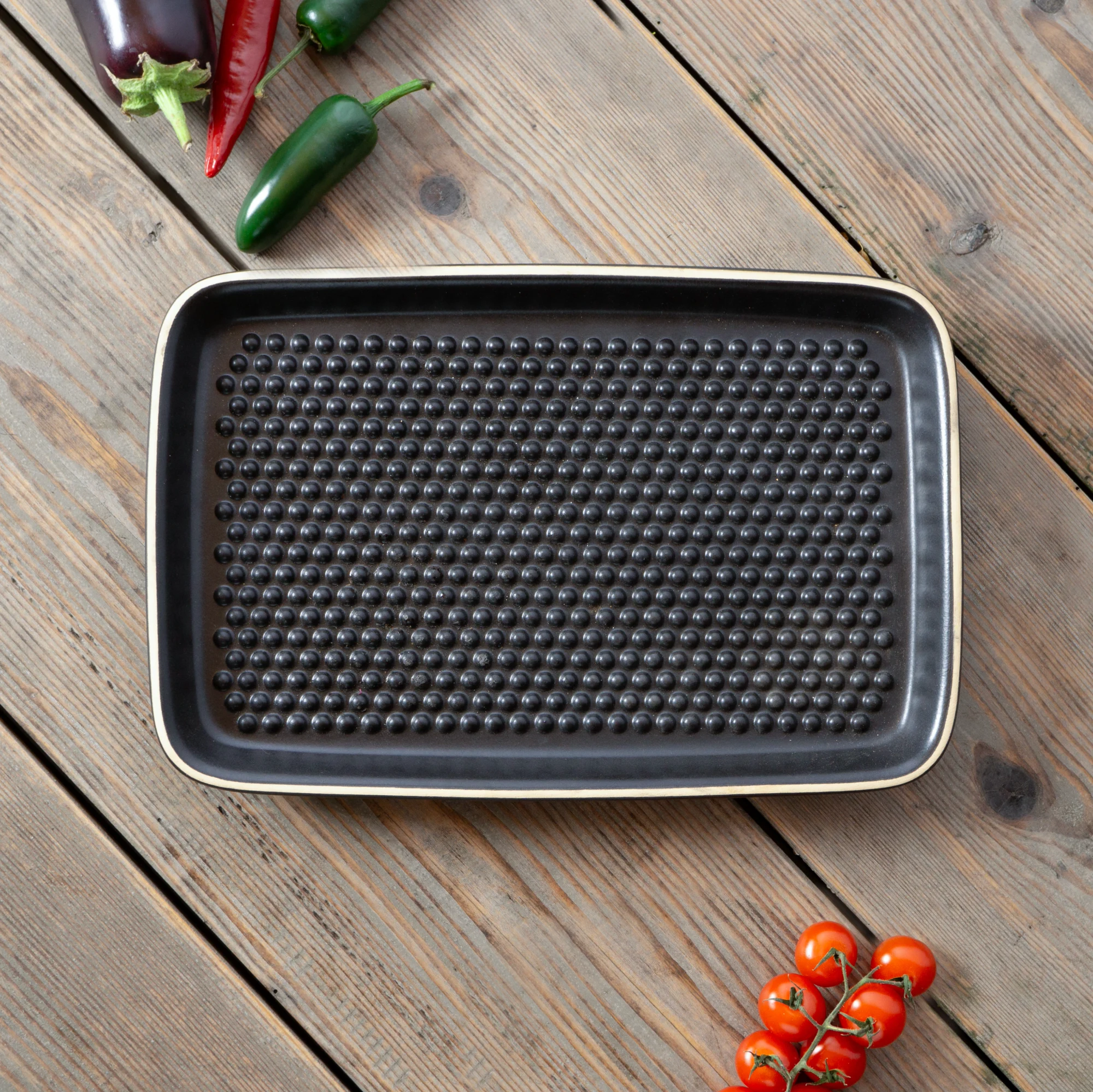 RÖMERTOPF Grillplancha Black – Hochwertige schwarze Grillplatte aus Keramik für gesundes Grillen Schwarze Römertopf Grill-Plancha aus Keramik in rechteckiger Form mit zwei seitlichen Griffmulden, auf heller Oberfläche stehend.