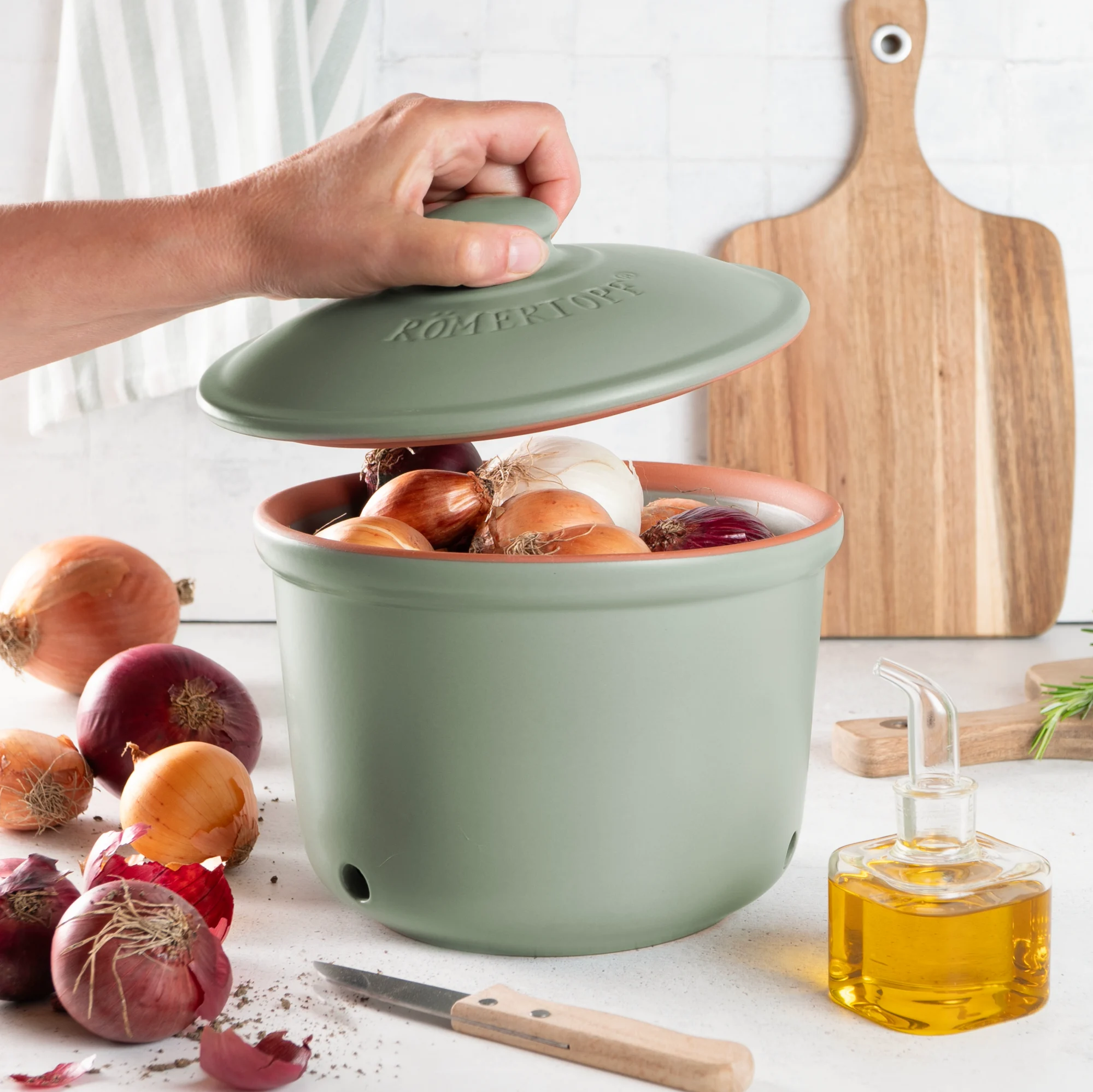 Römertopf Zwiebel-Topf grün – atmungsaktive Vorratsdose aus Keramik für längere Frische Grüner Römertopf-Frischetopf mit Deckel zur Aufbewahrung von Zwiebeln, aus Keramik, mit seitlichen Luftlöchern und eingeprägtem Schriftzug "Zwiebeln" auf der Vorderseite, vor neutralem Hintergrund.