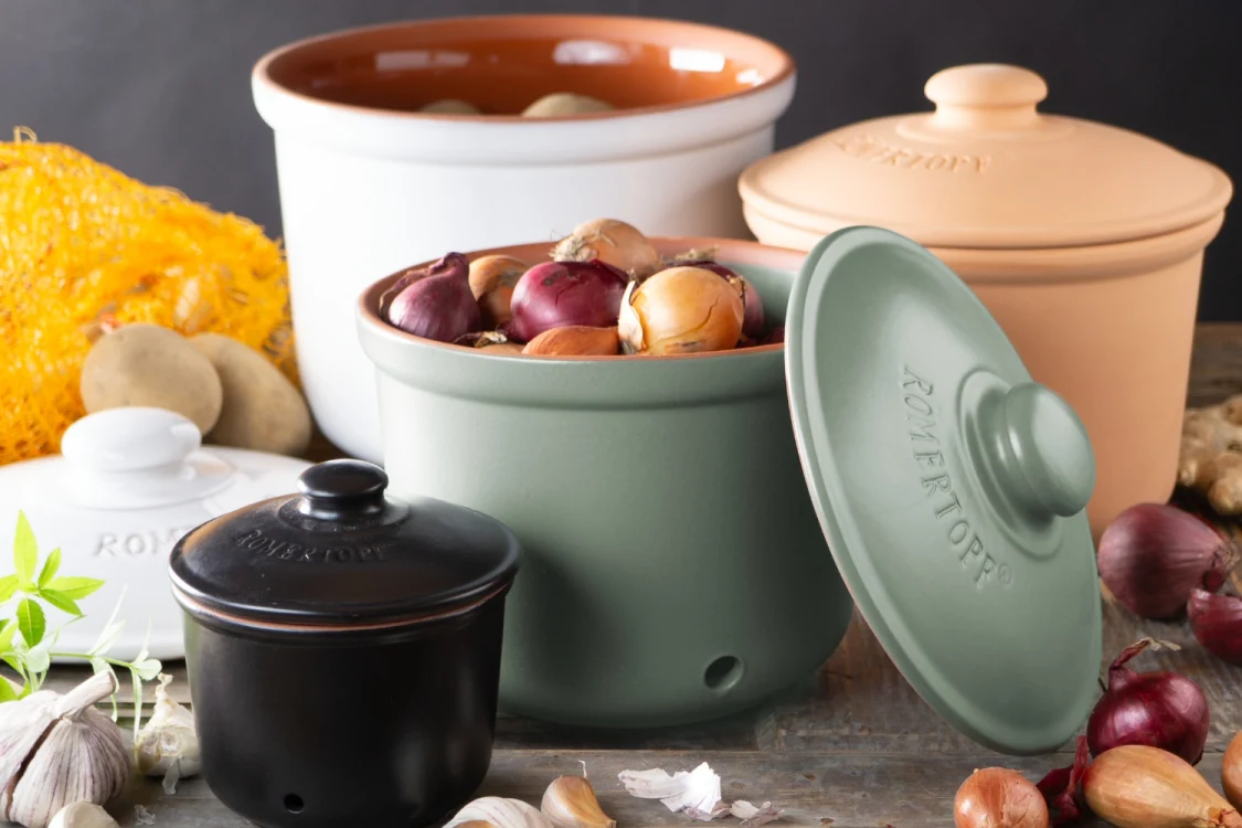 Rechteckige, weiße Frischebox aus Keramik mit Holzdeckel, darin gelagerte Tomaten; daneben eine aufgeschnittene Tomate auf einem hellen Untergrund.
