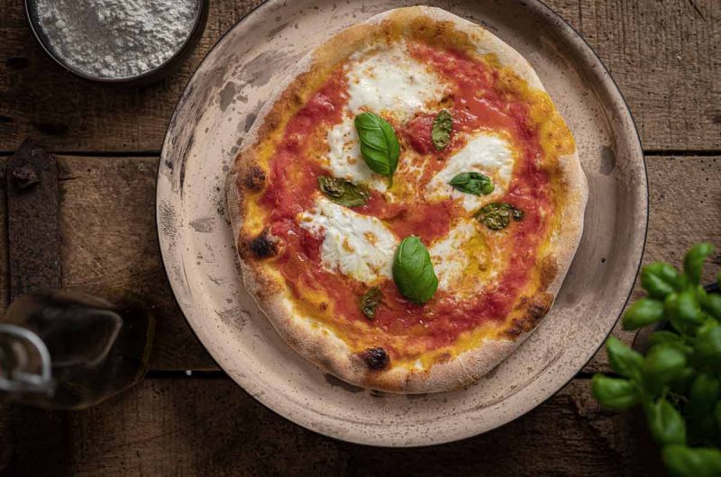 Pizza Margherita auf Teller mit Tomatensoße, Mozzarella und Basilikumblättern auf rustikalem Holztisch.