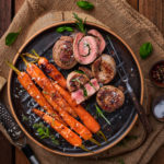 Gegrillte Rinderrouladen und glasiertes Gemüse auf rustikalem Teller, garniert mit Rosmarin und Meersalz.