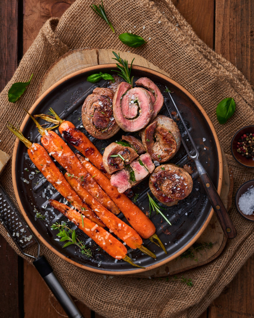 Gegrillte Rinderrouladen und glasiertes Gemüse auf rustikalem Teller, garniert mit Rosmarin und Meersalz.