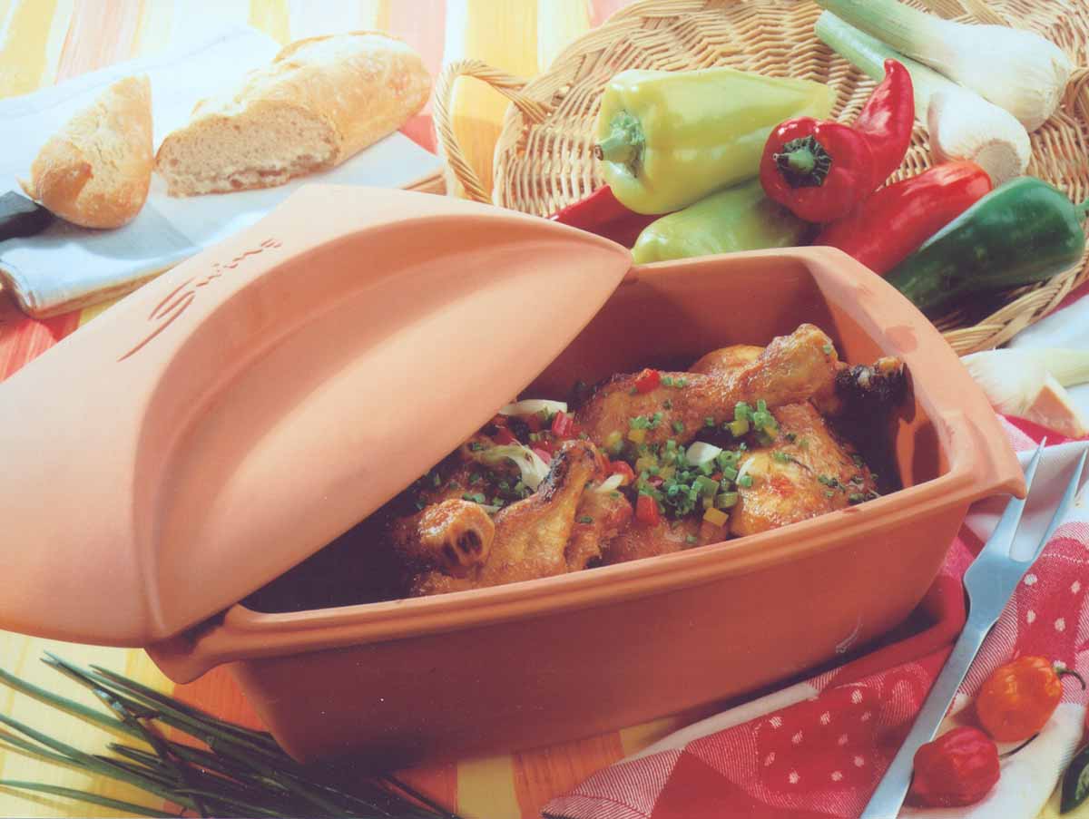 Hähnchen im Bräter mit Paprika, Zwiebeln und Brot im Hintergrund auf einem gedeckten Tisch.