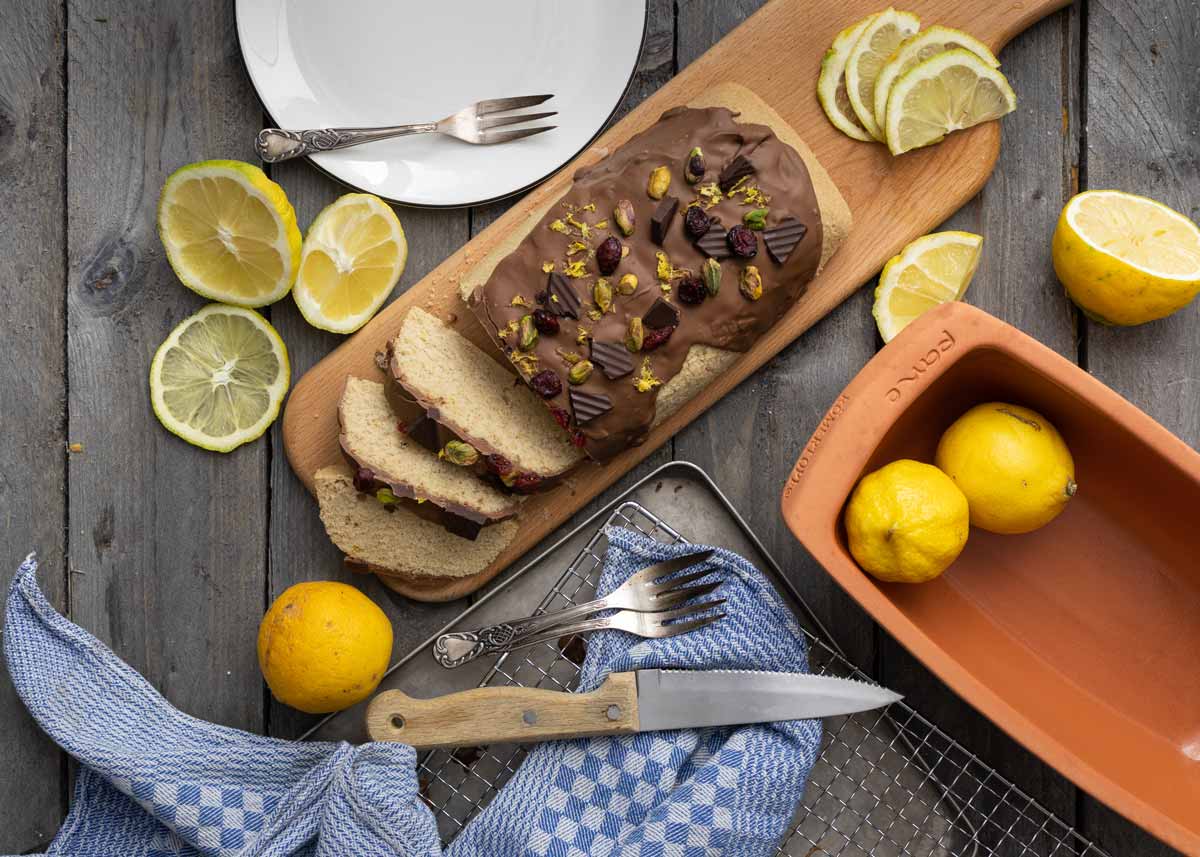 Gedeckter Tisch mit Zitronen, Messer und Gabel, angeschnittenem Schokokuchen mit Nüssen und Beeren auf Holzbrett.