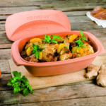 Schmortopf mit gebratenem Hähnchen und Orangen, garniert mit frischer Petersilie auf einem rustikalen Holztisch.