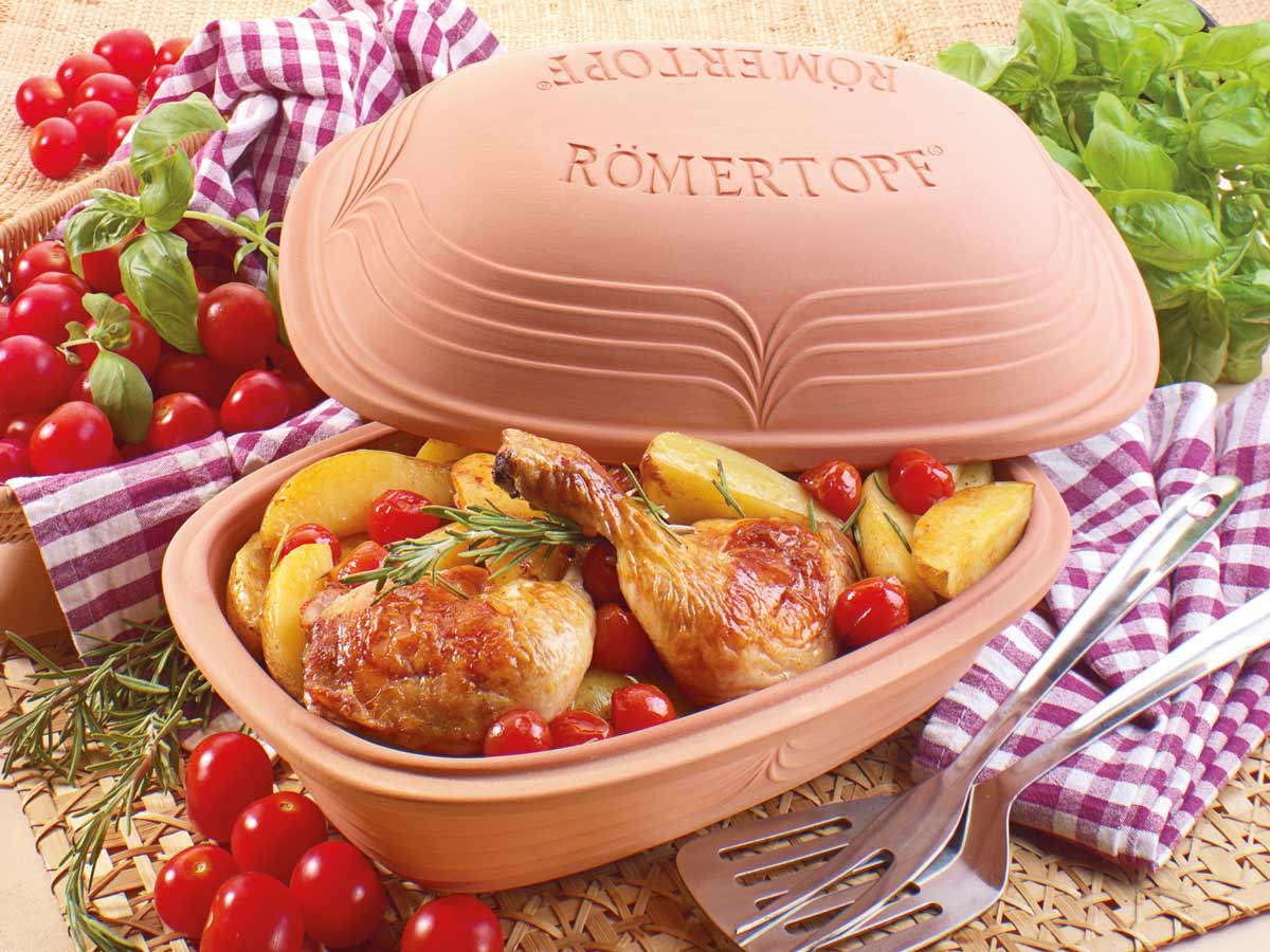Römertopf mit gebackenem Hähnchen, Kartoffeln und Tomaten, daneben frische Tomaten und Basilikum auf kariertem Tuch.