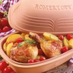 Brathähnchenkeulen mit Kartoffeln und Tomaten im Römertopf, dekoriert mit Rosmarin, auf einem karierten Tuch.