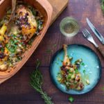 Brathähnchen mit Gemüse in einer Backform, serviert auf einem Teller. Gabel, Messer und Kräuter daneben.