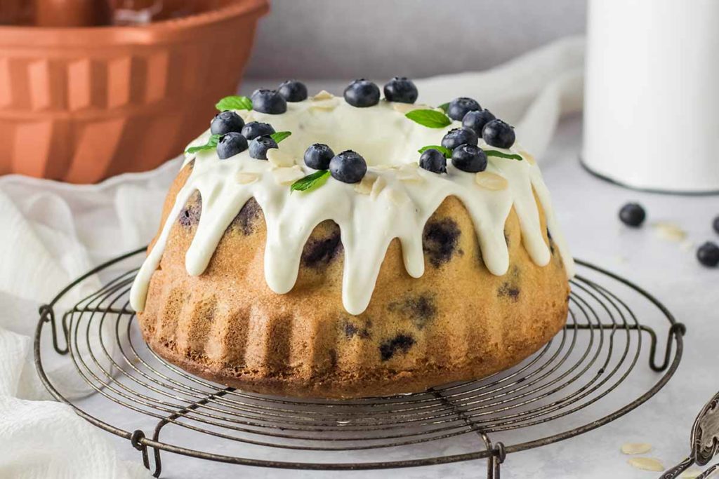 Gugelhupf mit weißem Zuckerguss, Blaubeeren und Minzblättern auf einem Drahtgitter serviert.