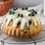 Gugelhupf mit weißem Zuckerguss, Blaubeeren und Minzblättern auf einem Drahtgitter serviert.