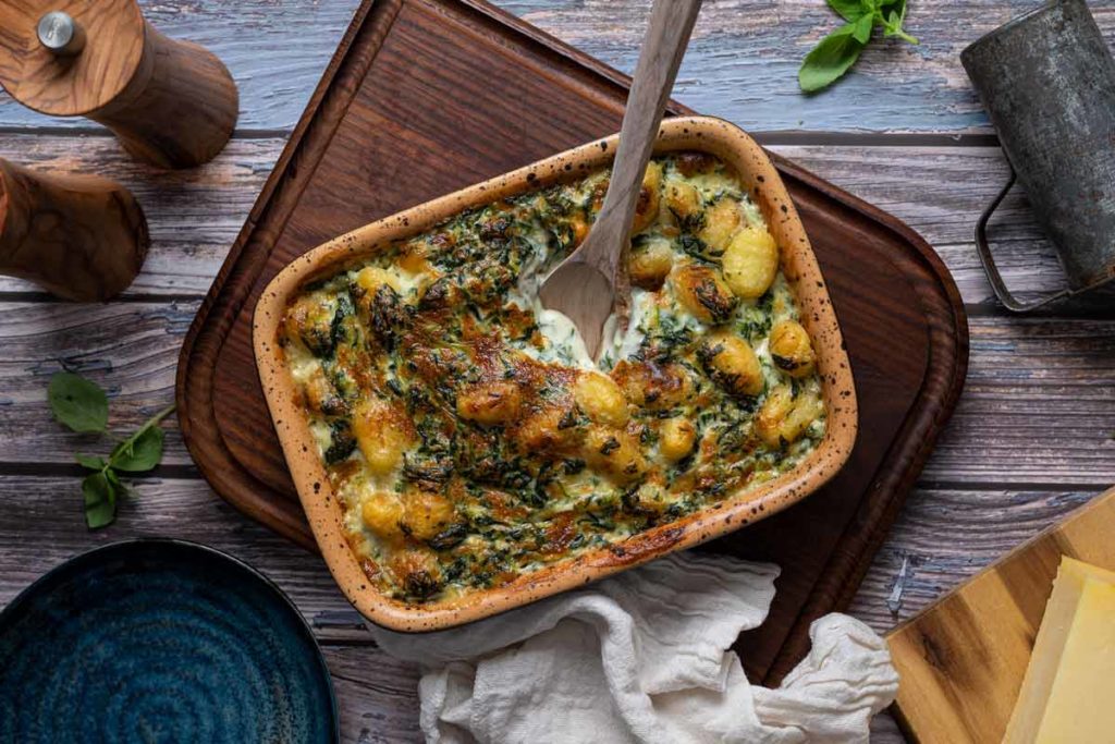 Ofen-Gnocchi in einer rechteckigen Auflaufform mit Spinat und Käse überbacken, auf einem Holzbrett serviert.