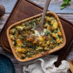 Ofen-Gnocchi in einer rechteckigen Auflaufform mit Spinat und Käse überbacken, auf einem Holzbrett serviert.