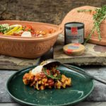 Keramikbräter mit Reisgericht, Zitronenspalten, Pfeffer, Rosmarin; grüner Teller mit Portion, Löffel, Gabeln.