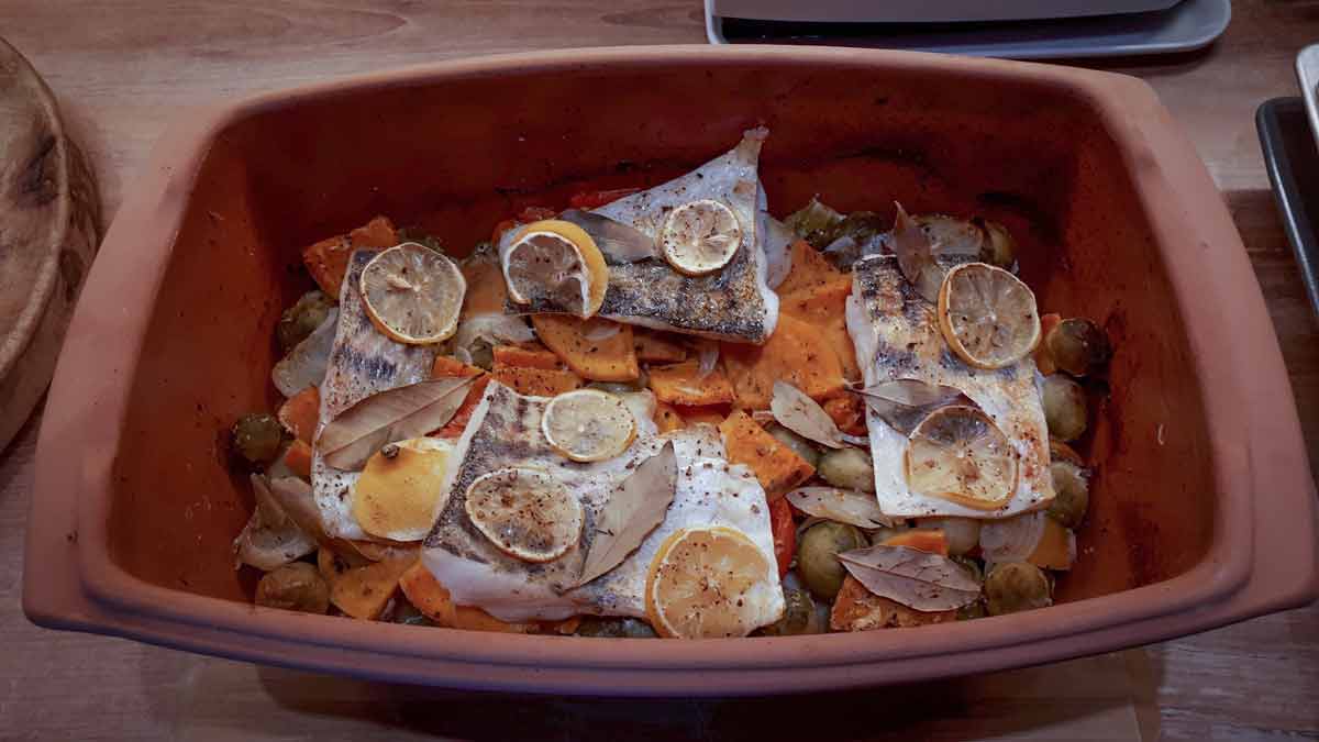 Gebackener Fisch in Auflaufform mit Zitronenscheiben, Lorbeerblättern, Kürbis und Rosenkohl.